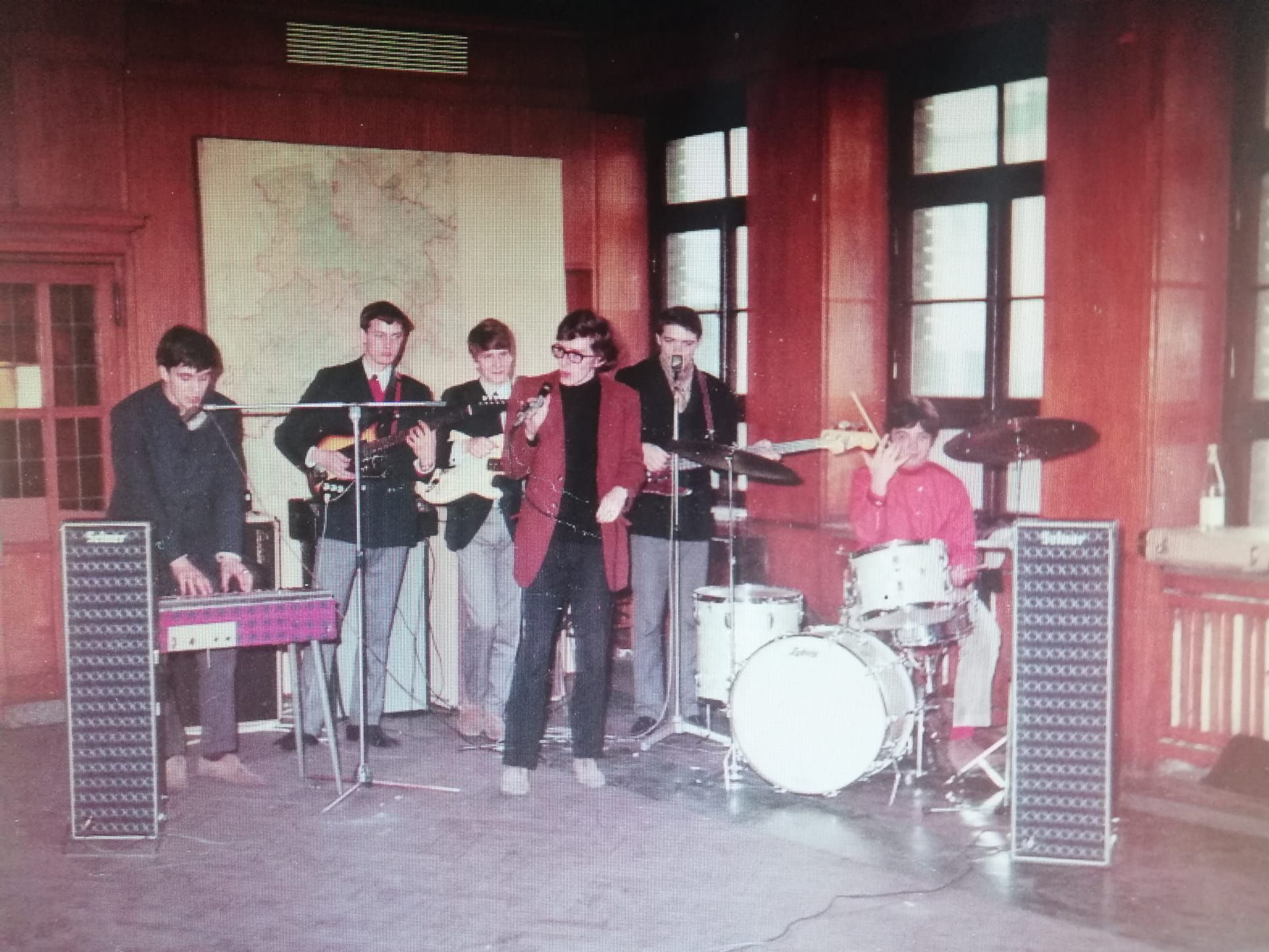 Eine Band ist in Aktion zu sehen. Ein Mann im roten Blazer singt.