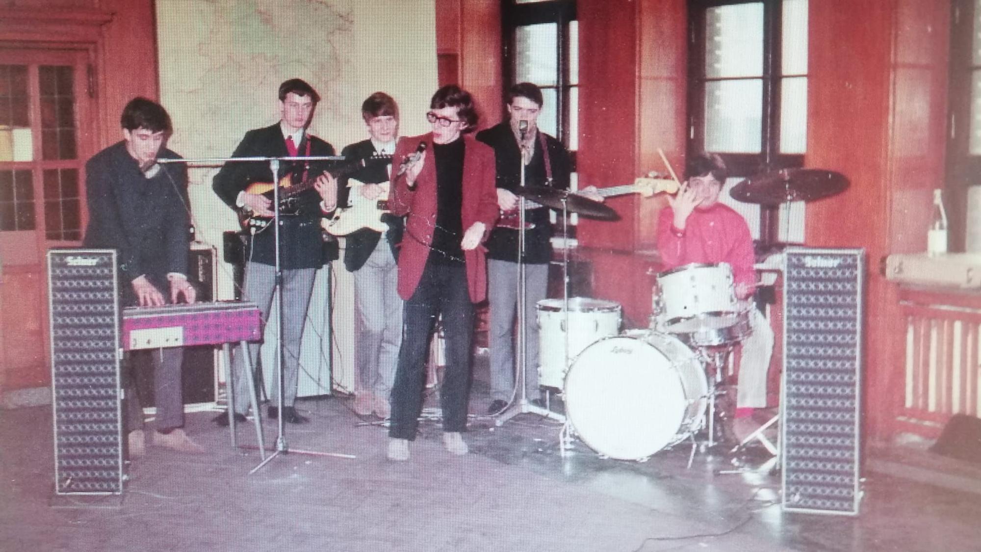 Eine Band ist in Aktion zu sehen. Ein Mann im roten Blazer singt.