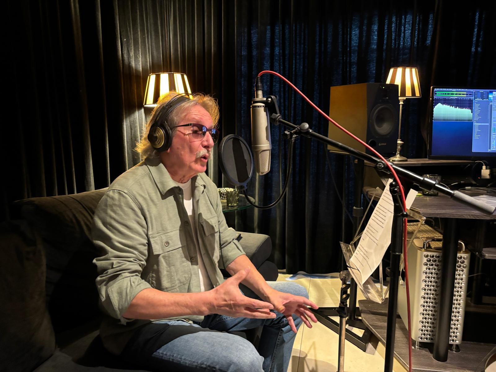 Ein Mann sitzt in einem Aufnahmestudio und singt ins Mikro.