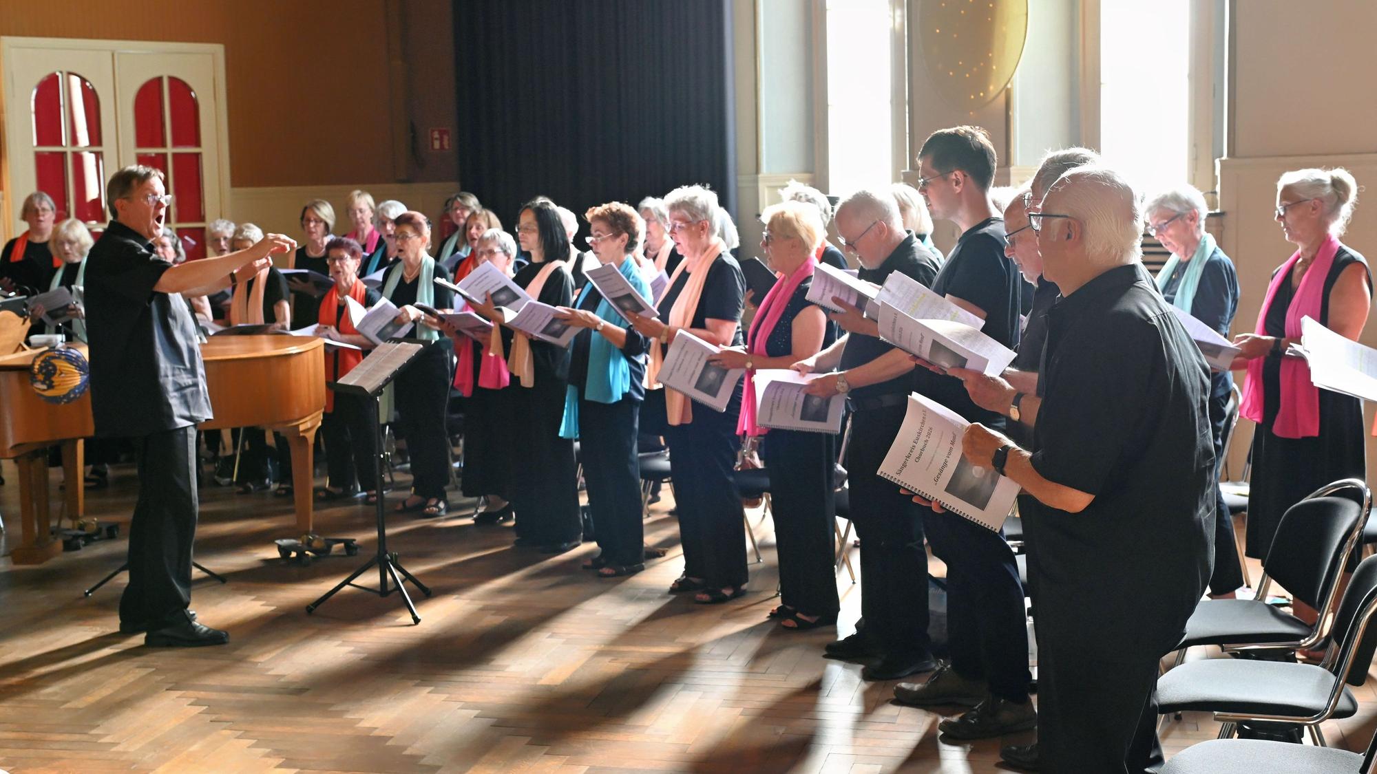 Eine Gruppe von Männern und Frauen steht in einem Halbkreis und singt.