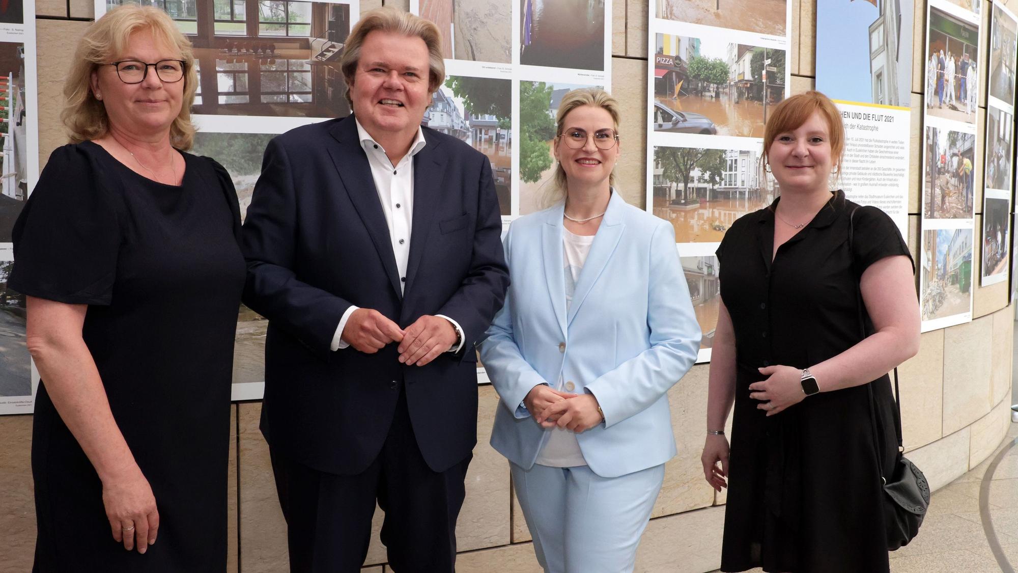 Klaus Voussem steht mit drei Damen vor Bildern einer Ausstellung.