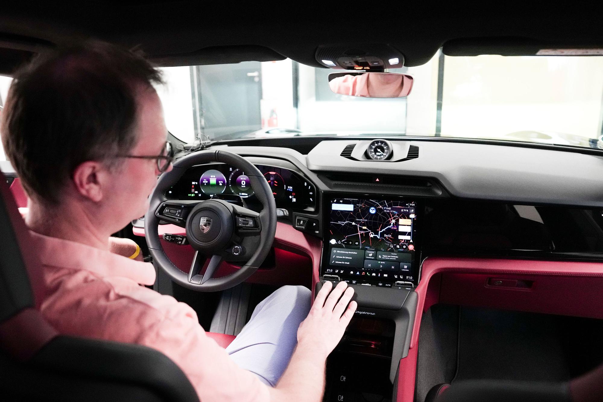 Ein Mann sitzt hinter dem Steuer eines Sportwagens und schaut auf das große Digital-Display neben dem Lenkrad.