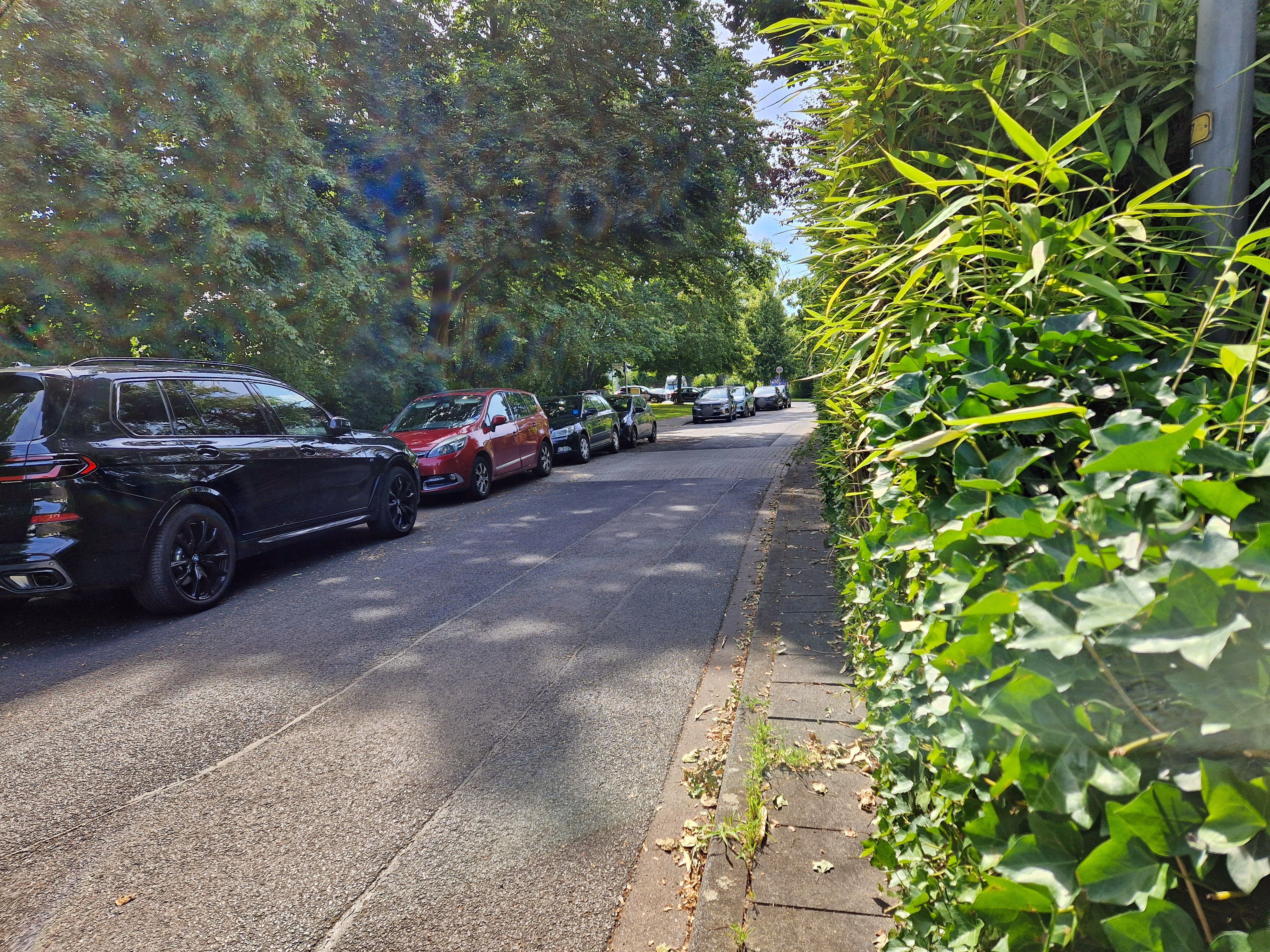 An einer sehr schmalen Straße stehen abgestellte Autos.