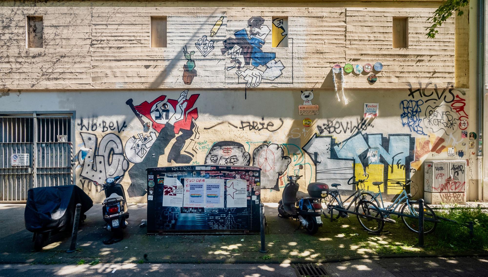 Auf einer Hauswand sind zahlreiche Wandbilder, aber auch lieblose Farbschmierereien hinterlassen worden.
