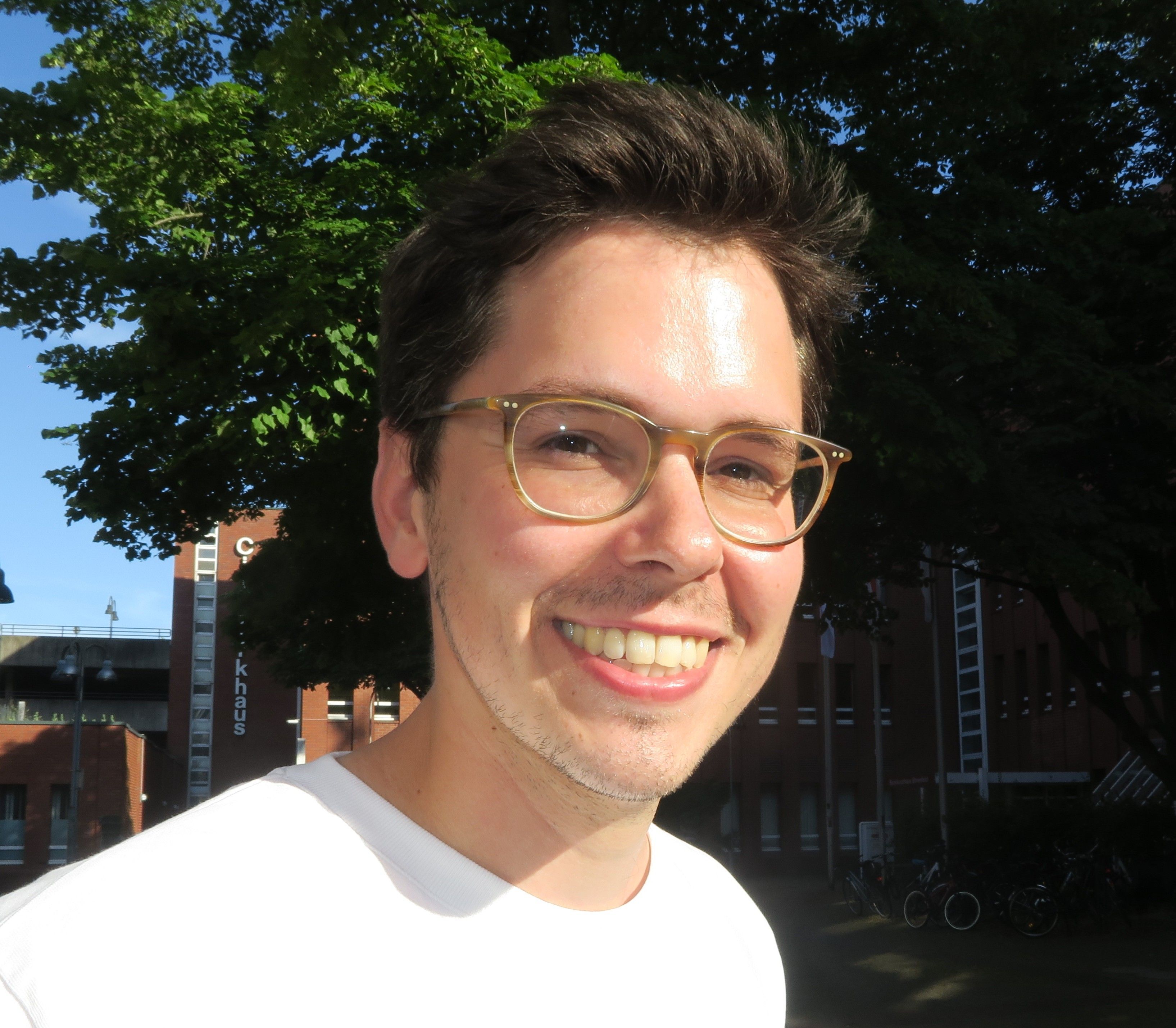 Ein junger Mann  mit Brille und dunklem Haar blickt lachend in die Kamera.