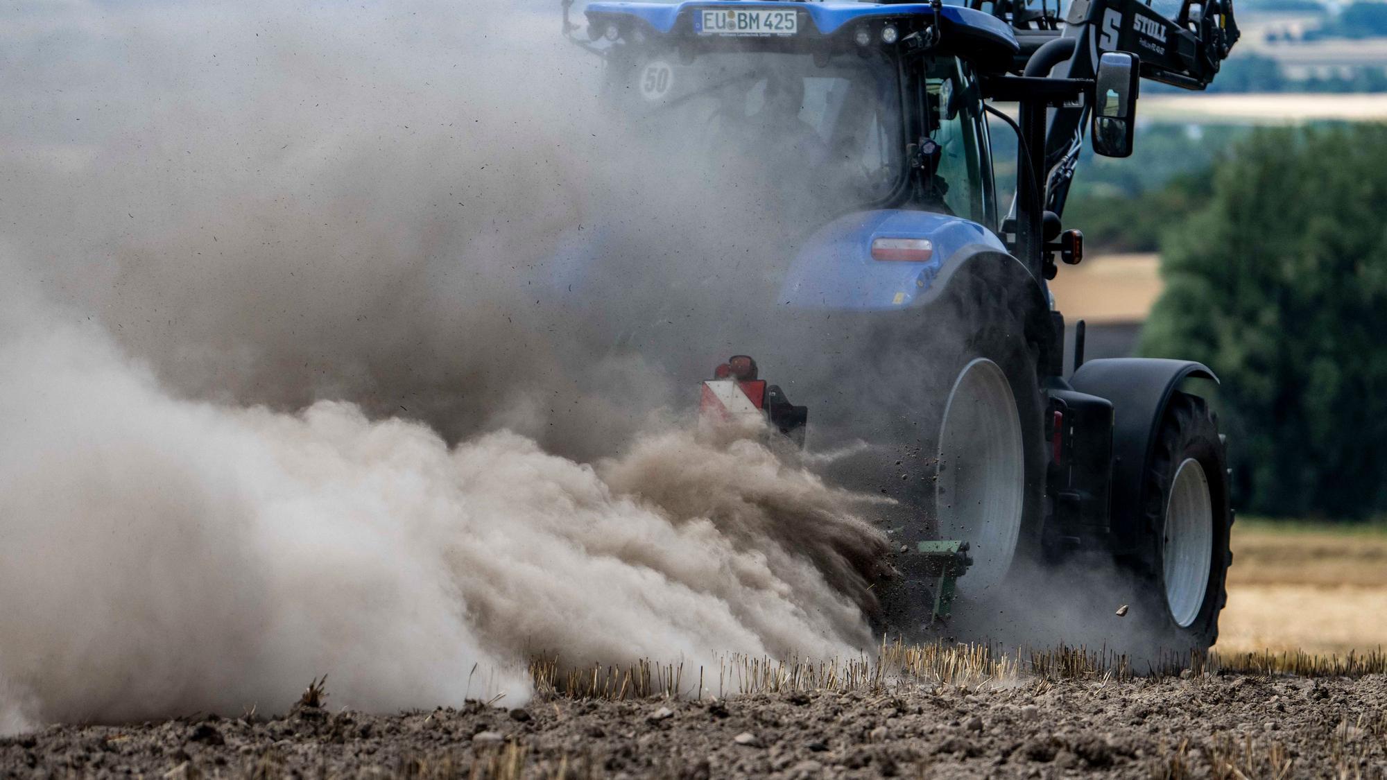 Ein blauer Traktor fährt über ein Stoppelfeld, von dem Rauch aufsteigt.