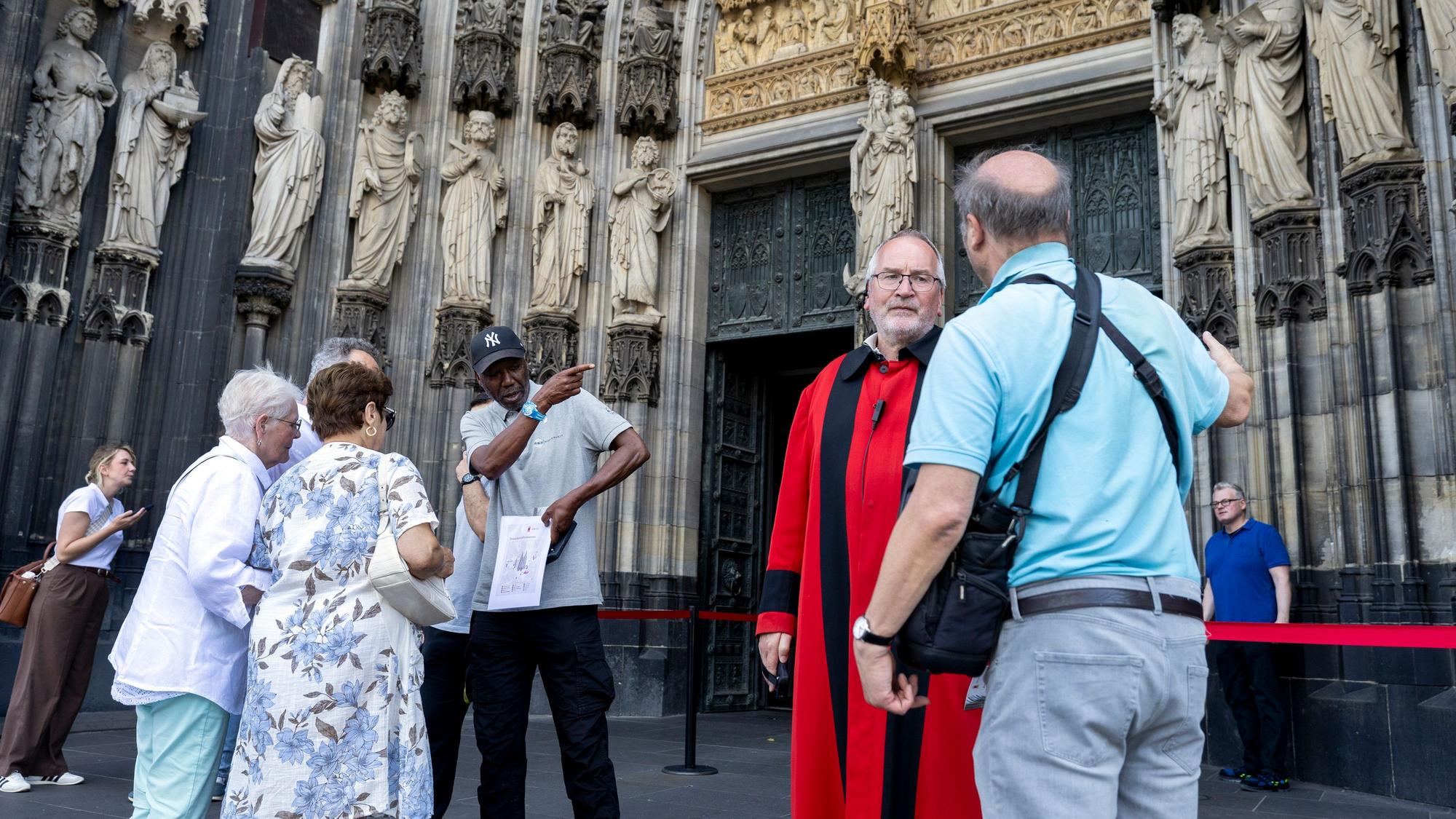 Domschweizer und Servicekräfte informieren Menschen vor dem Kölner Dom über die neuen Besuchsregeln.