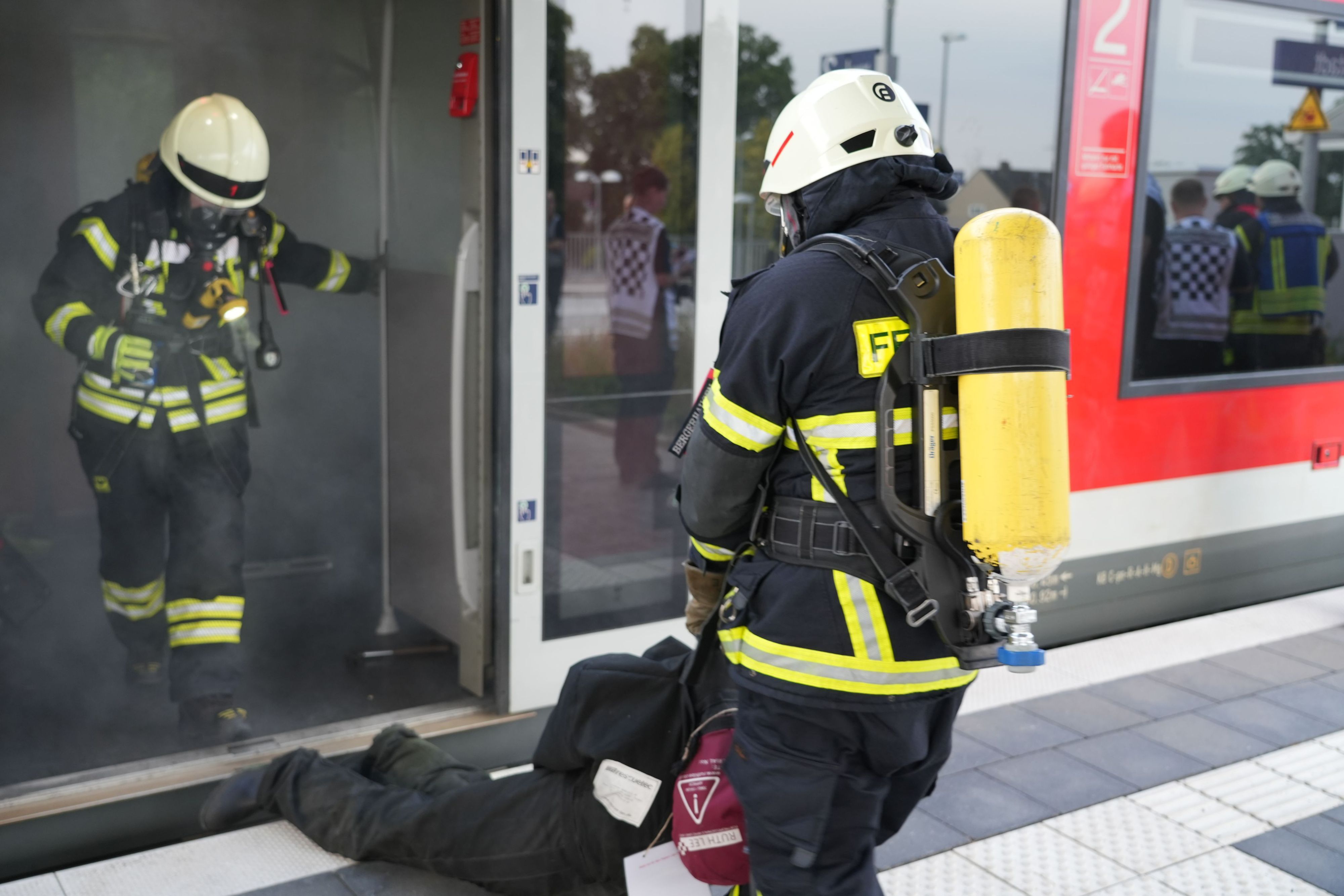 Eine Feuerwehrkraft zieht einen Mann aus einem qualmenden Zugabteil.
