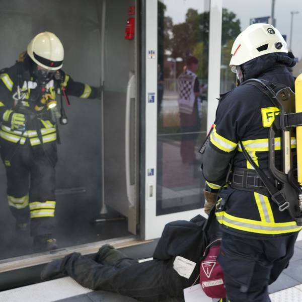 Eine Feuerwehrkraft zieht einen Mann aus einem qualmenden Zugabteil.
