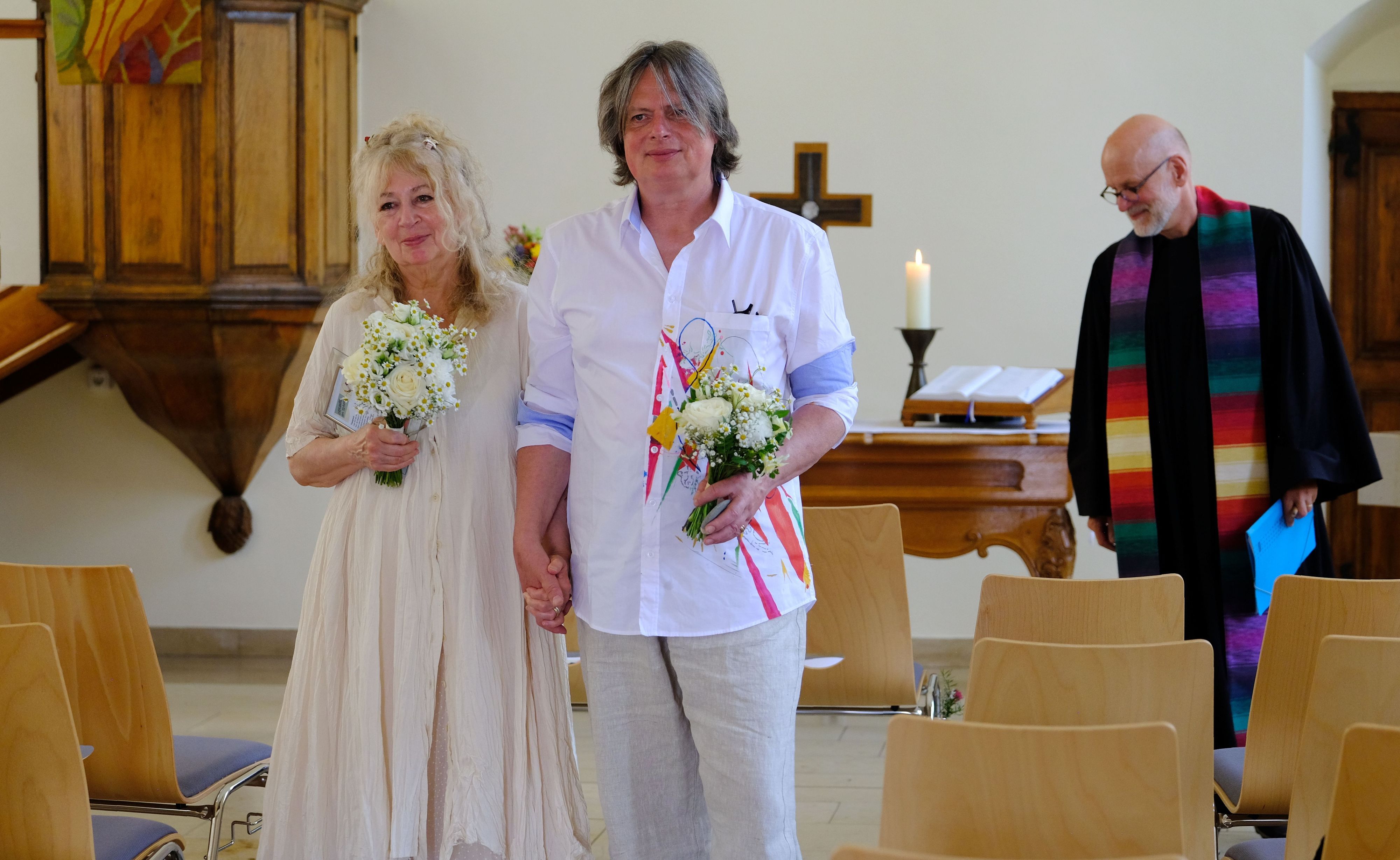 Stephan Everling und Maf Räderscheidt gehen in sommerlicher Kleidung und mit Blumensträußen vom Altar zum Eingang der Kirche.