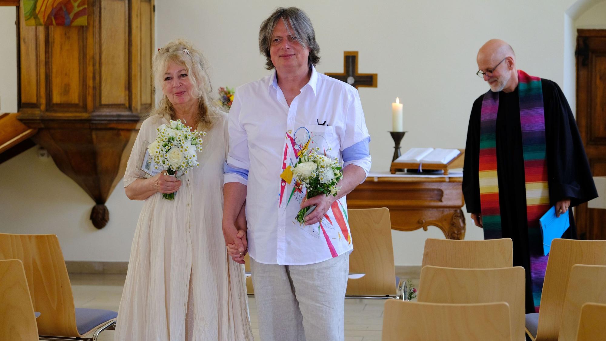 Stephan Everling und Maf Räderscheidt gehen in sommerlicher Kleidung und mit Blumensträußen vom Altar zum Eingang der Kirche.