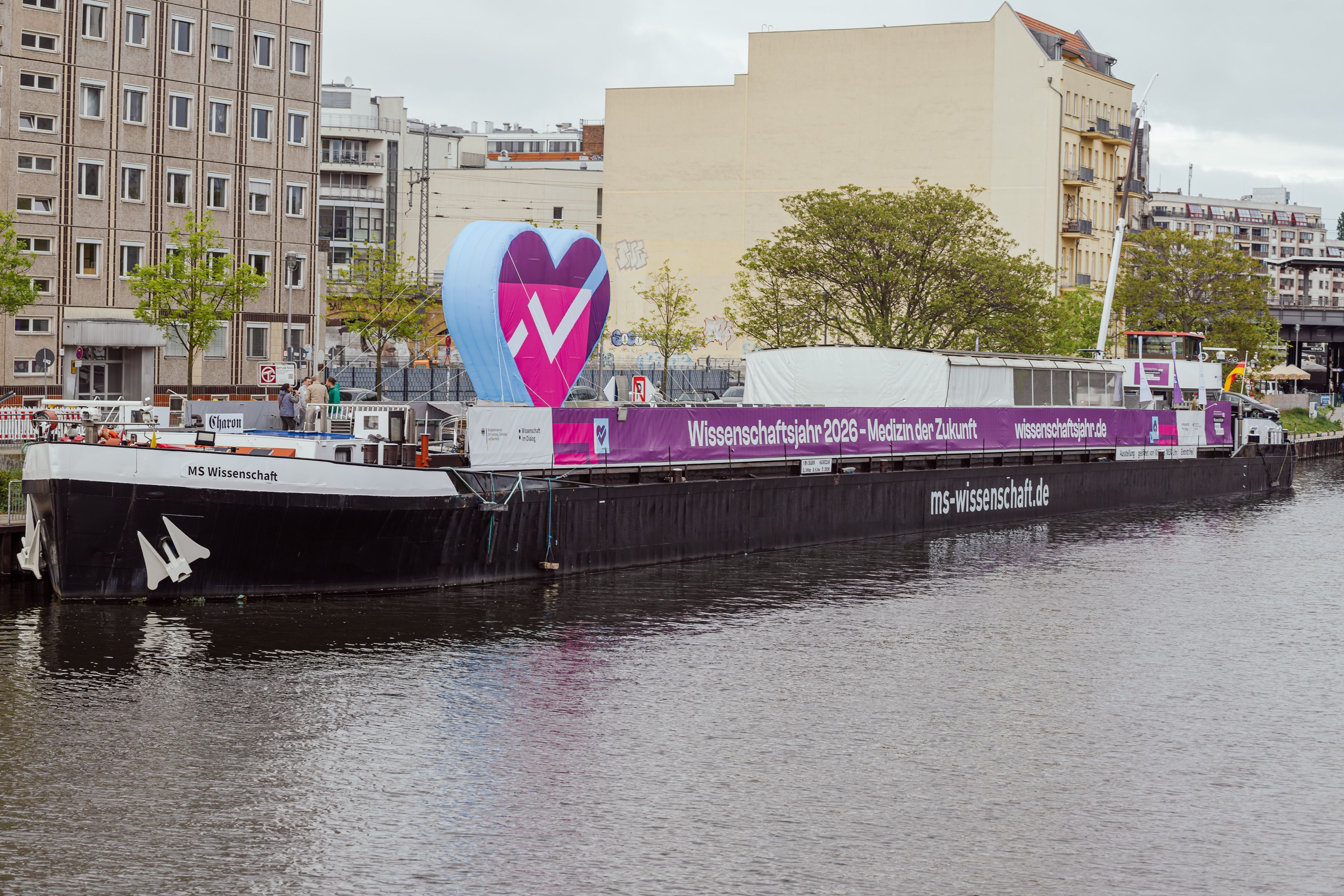 Ein großes Schiff auf dem Wasser liegt am Hafen, im Hintergrund Häuser.