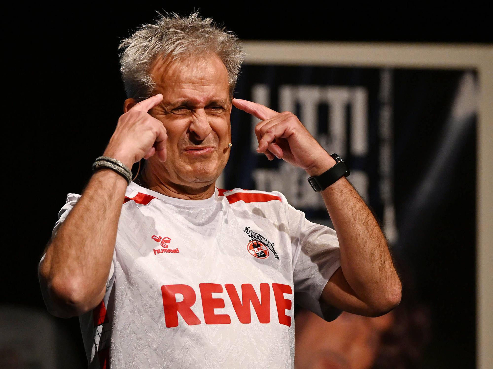 Pierre Littbarski im FC-Trikot, er hält sich beide Zeigefinger an den Kopf.
