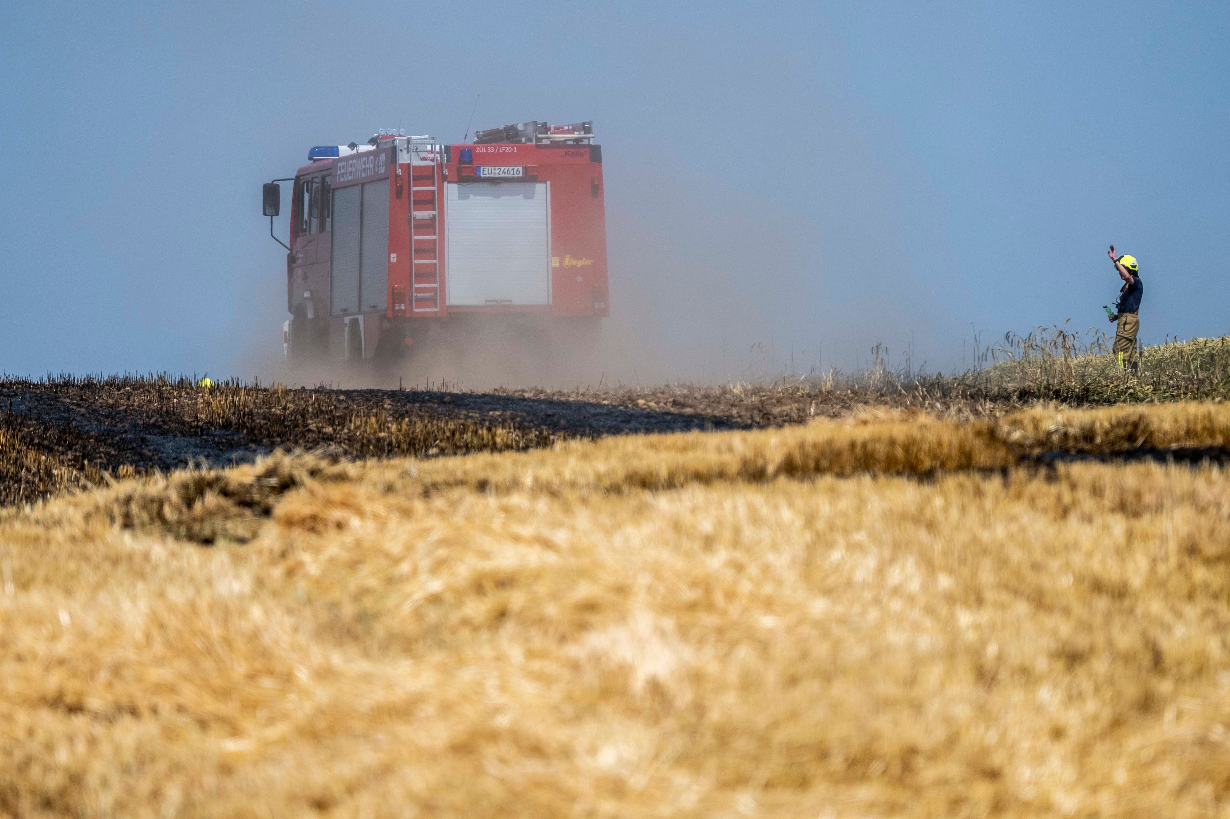 Ein Feuerwehrauto fährt über ein Feld. Im Vordergrund sind Stoppeln gelb, dahinter schwarz verkohlt.