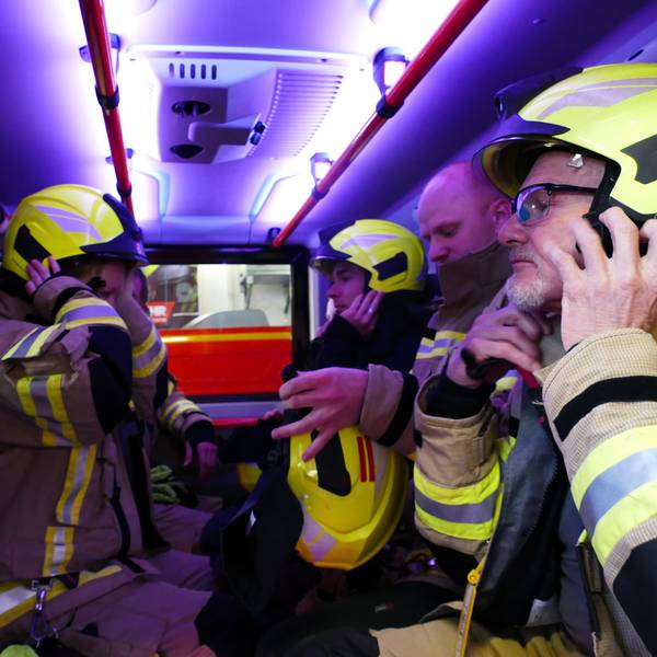 Auf der Fahrt zum Einsatzort setzen die Feuerwehrleute ihre Helme auf und streifen sich die Atemschutzgeräte über.