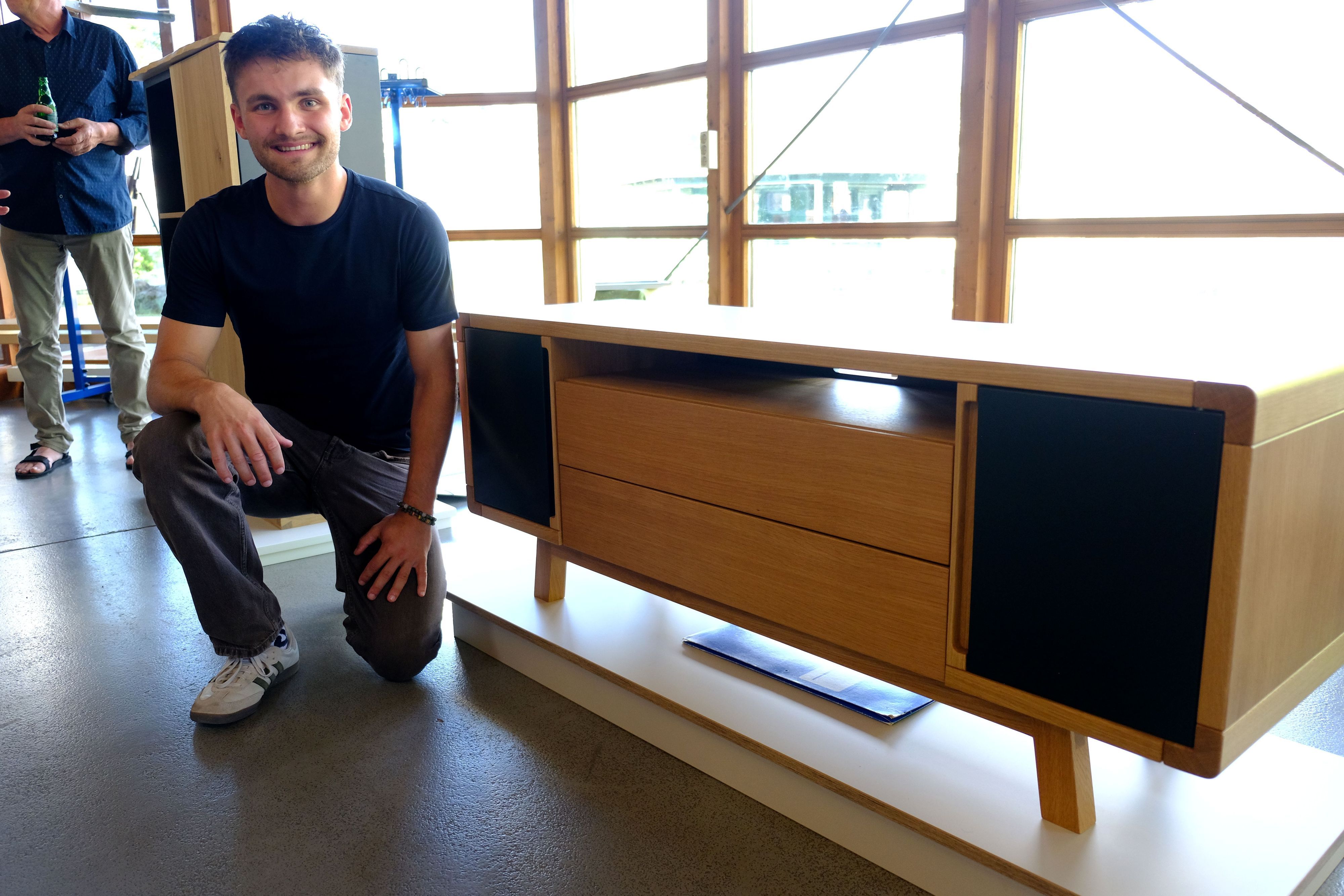 Jan Beyers kniet neben einem Sideboard mit Massivholzdetails, das vor einer Fensterfront steht.