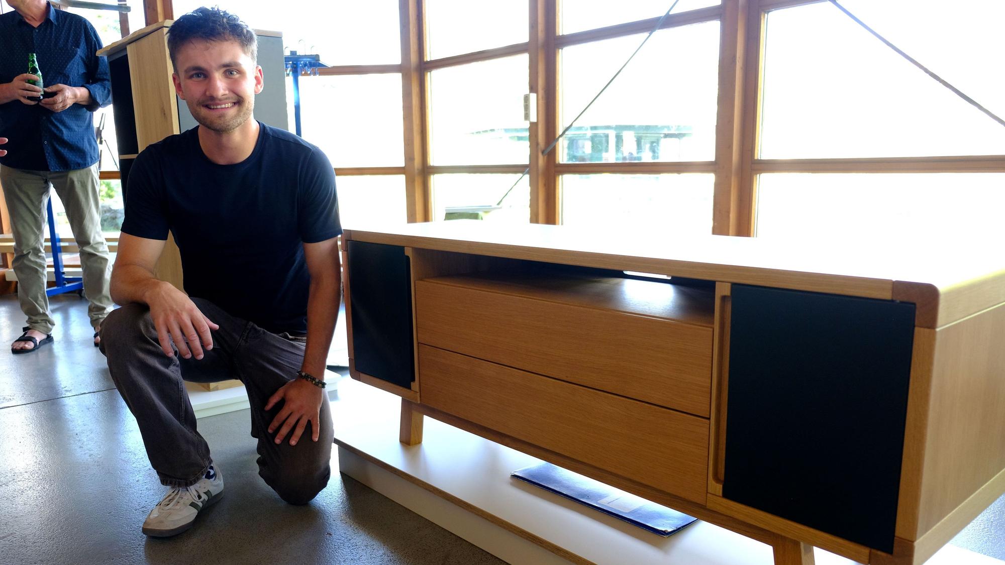 Jan Beyers kniet neben einem Sideboard mit Massivholzdetails, das vor einer Fensterfront steht.