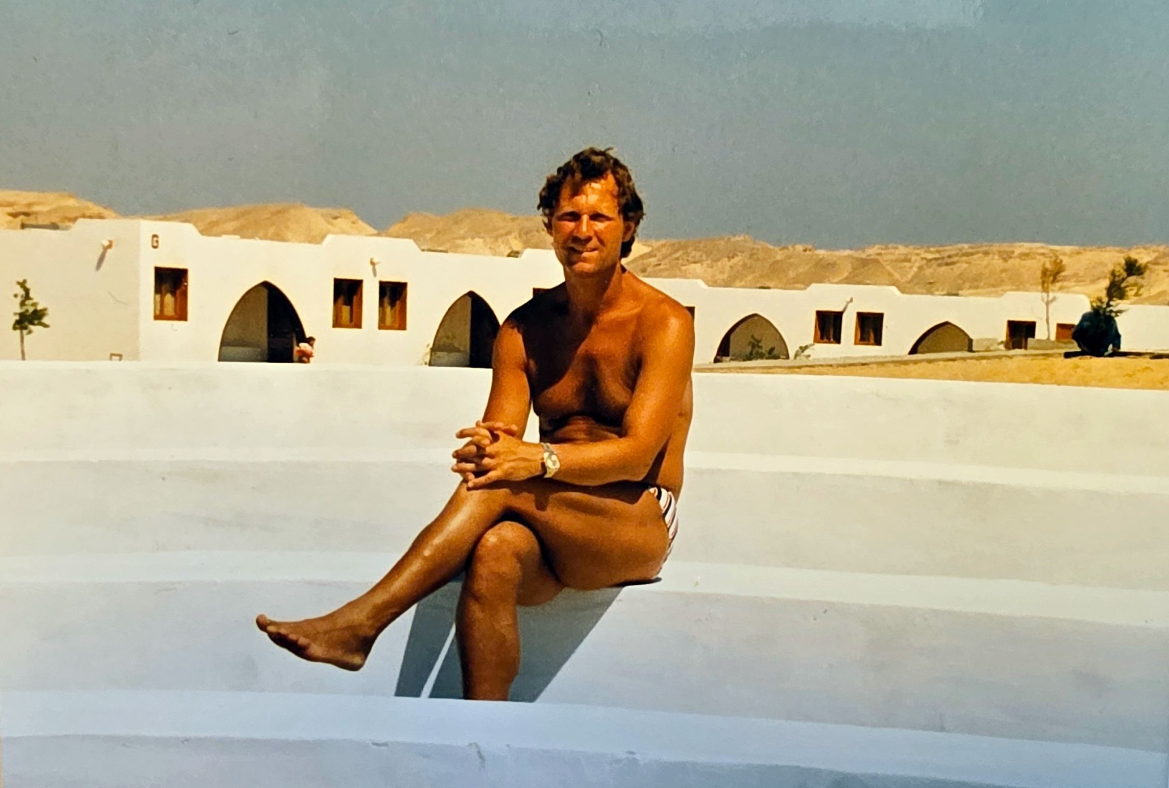 Ein junger Mann sitzt an einem Pool ohne Wasser.