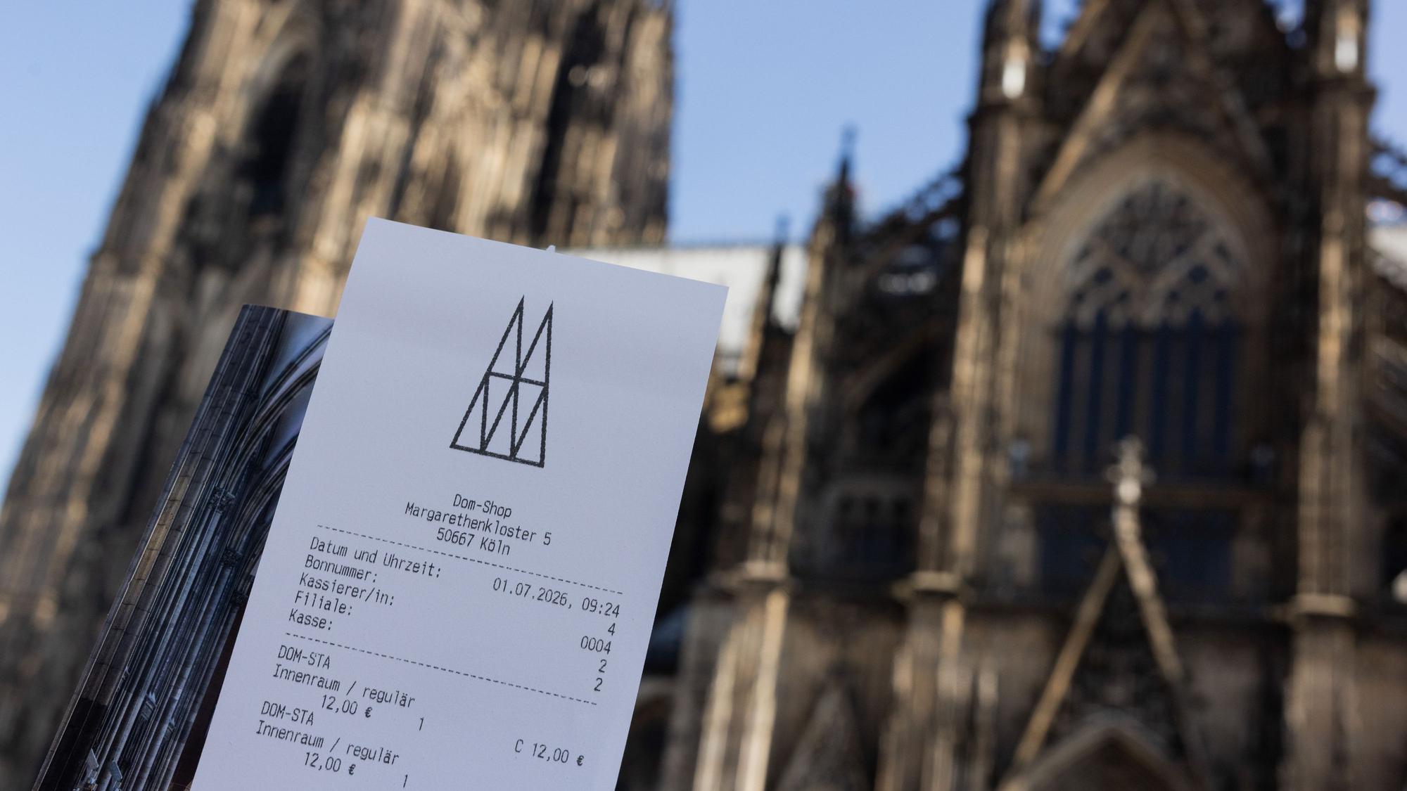 Eine Touristin zeigt ihr Ticket vor dem Kölner Dom. Der Eintritt in den Kölner Dom kostet ab dem 1. Juli zwölf Euro für Besucher. Betende sollen in einen bestimmten Bereich weiterhin kostenlos Zutritt erhalten. +++ dpa-Bildfunk +++