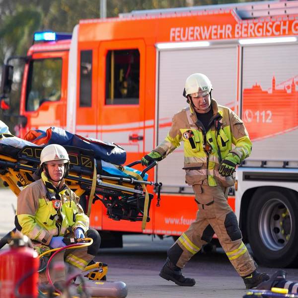 Ein Feuerwehrmann fährt eine Rettungstrage vor einem Löschfahrzeug vorbei.