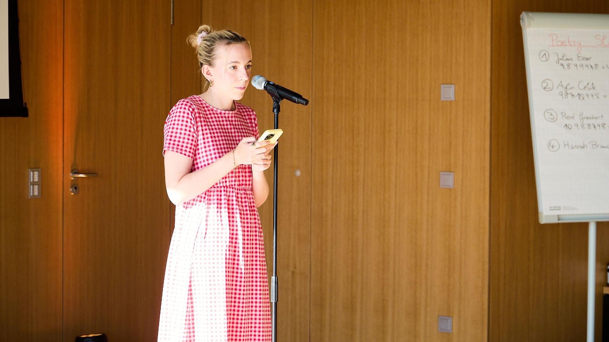 Hanna Braucks steht in rot-kariertem Kleid an einem Mikrofon.
