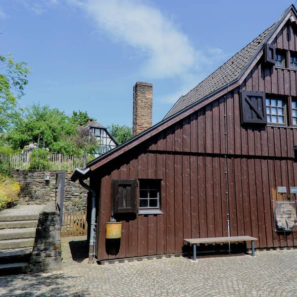 Eine Fassade eines großen mit Holz verkleideten Hauses, davor eine Bank
