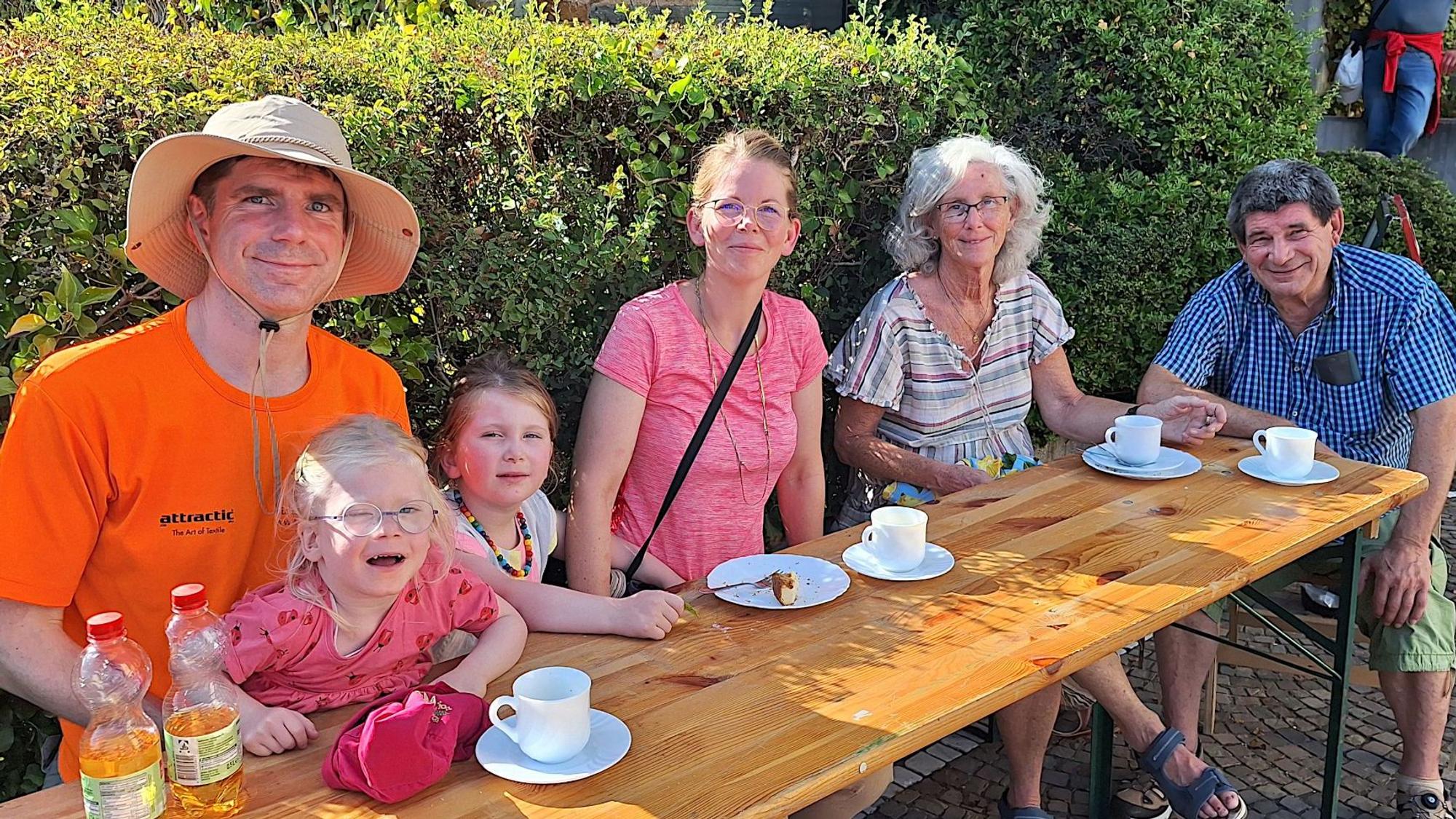 Die Familie sitzt an einem Bierzelttisch und trinke Kaffee und Apfelschorle.
