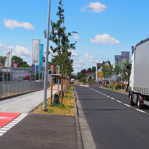 Auf der sanierten Römerallee fährt ein Lastwagen. Links steht eine Reihe Schwammstadtbäume.