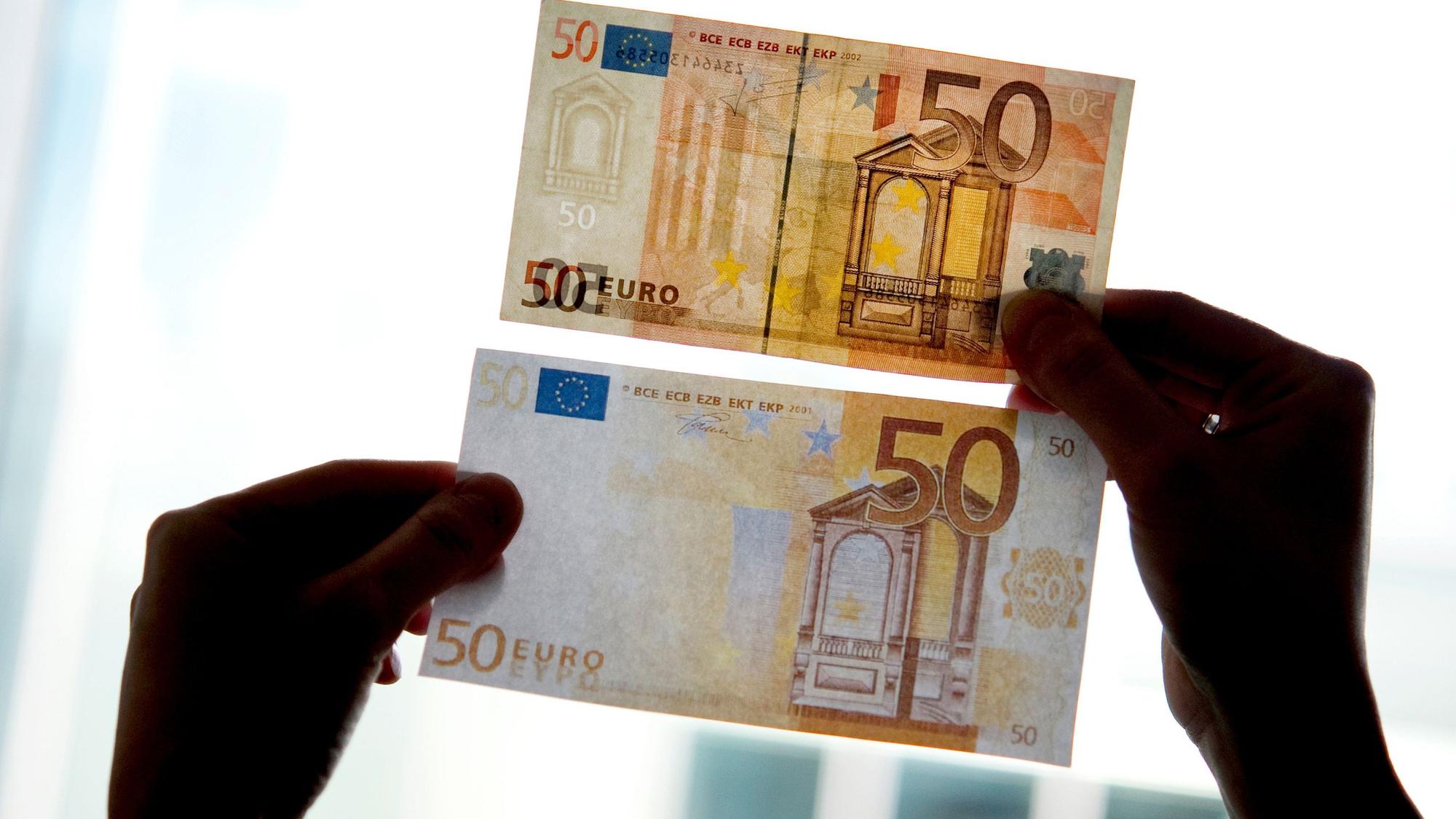 Ein echter und ein falscher Fünfzig-Euro-Schein werden gegen das Licht gehalten.