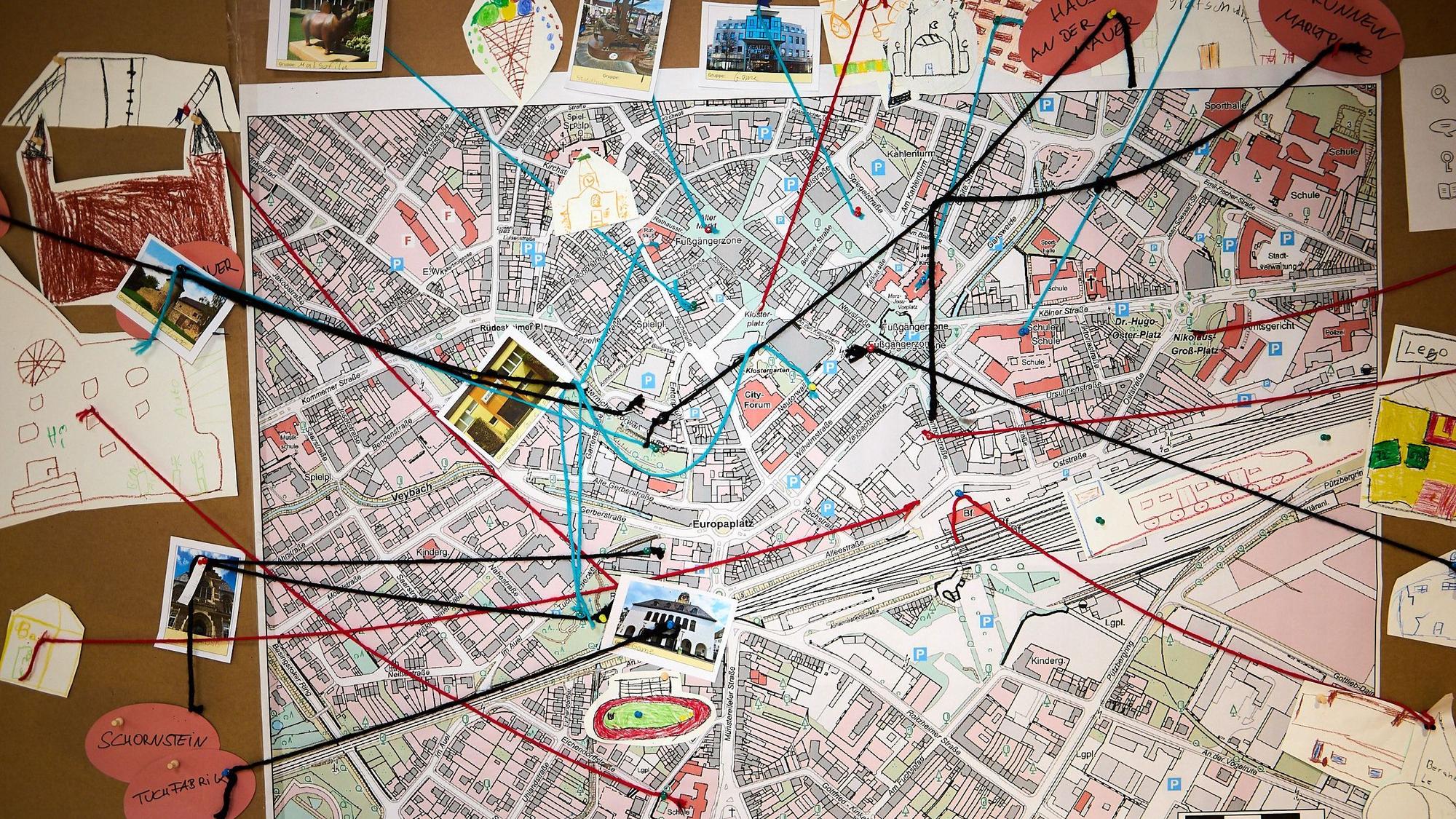 Auf einem großen Stadtplan von Euskirchen sind einige Orte mit Fotos und Wollfäden markiert.
