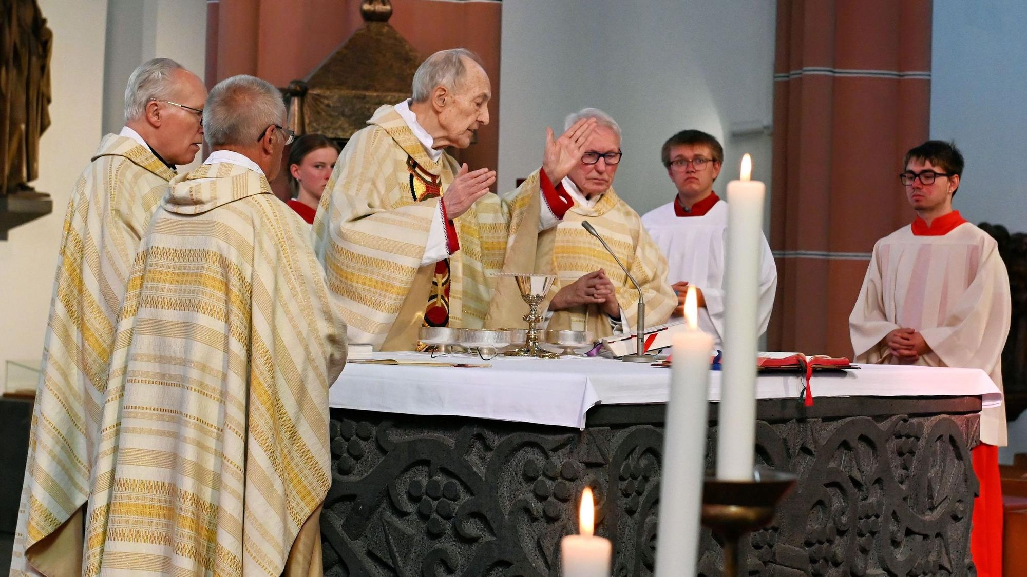 Vier Geistlilche stehen am Altar, Helmut Moll hebt segnend die Hand. Rechts sind zwei Messdiener zu sehen, im Vordergrund drei brennende Kerzen.
