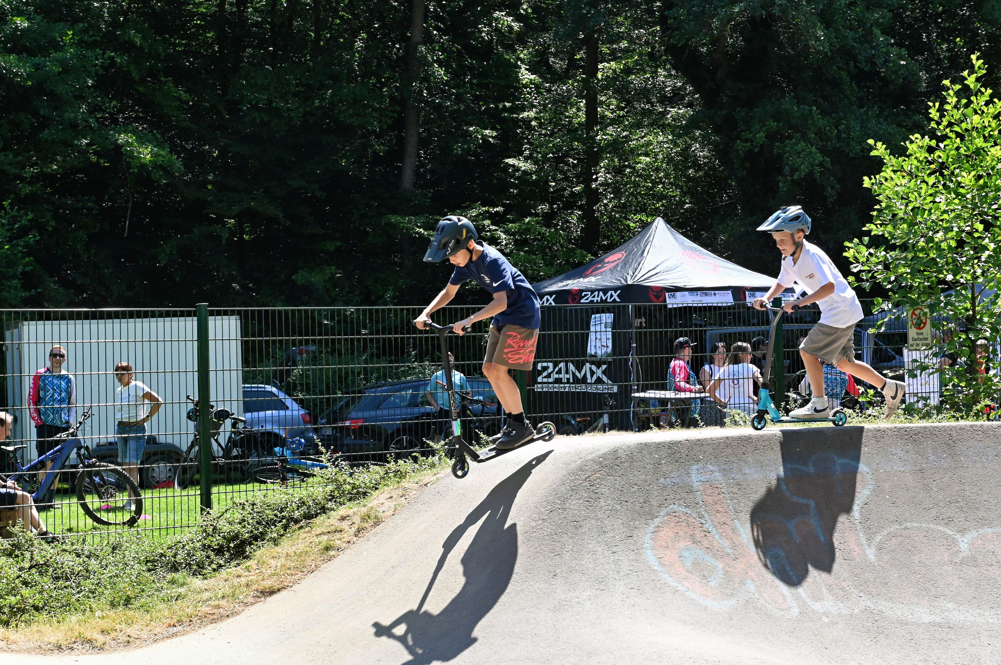 Die beiden Jungs befahren den Pumptrack in Kommern mit ihren City-Rollern.