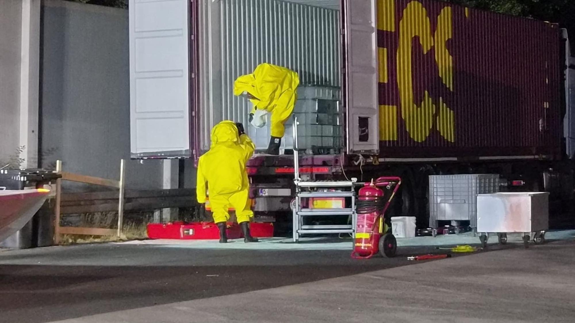 Das Bild zeigt zwei Feuerwehrleute, die unter großen Vorsichtsmaßnahmen die Container untersuchen.