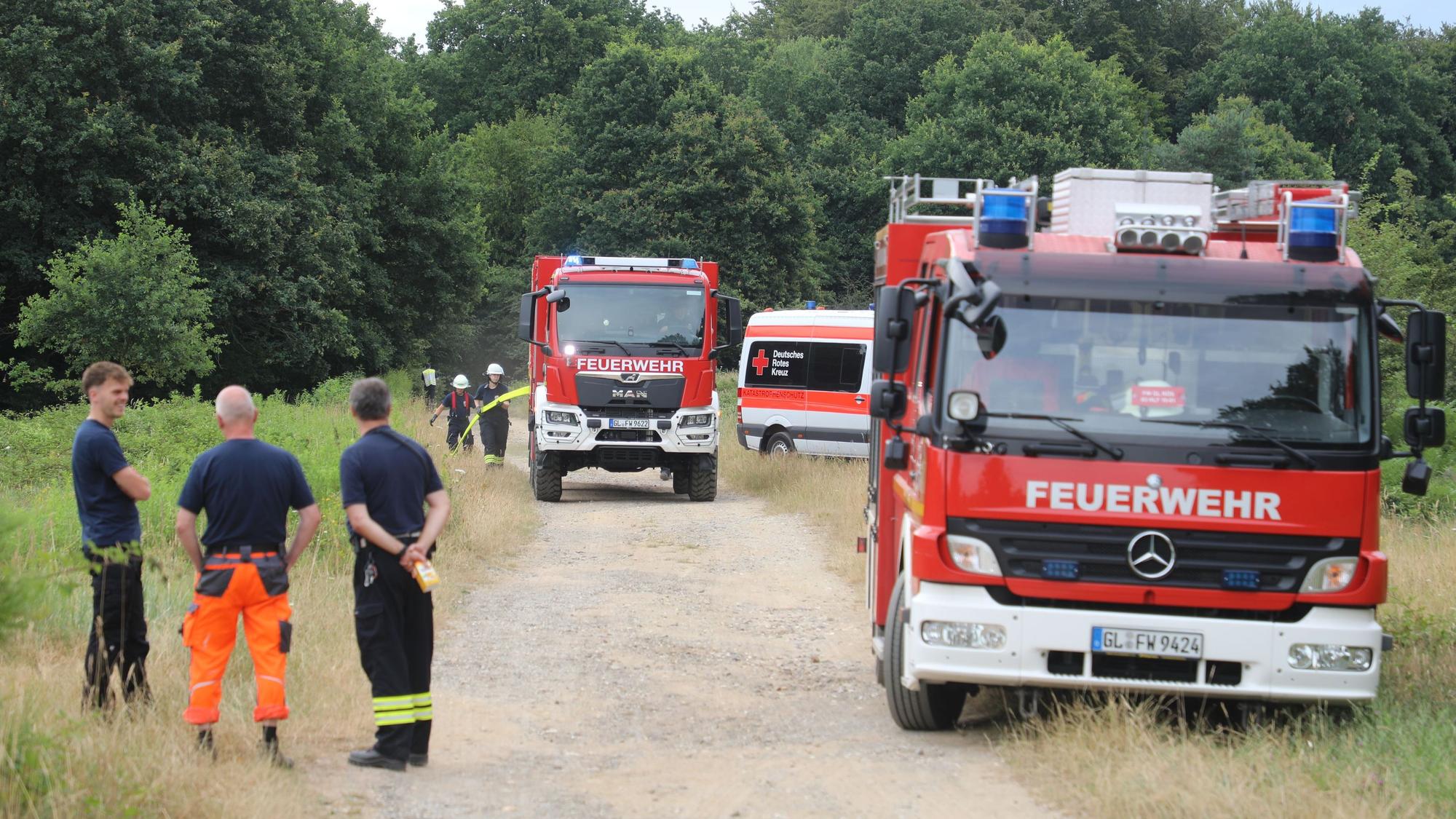 Zwei Feuerwehrautos und drei Männer der Feuerwehr auf einem Schotterweg.