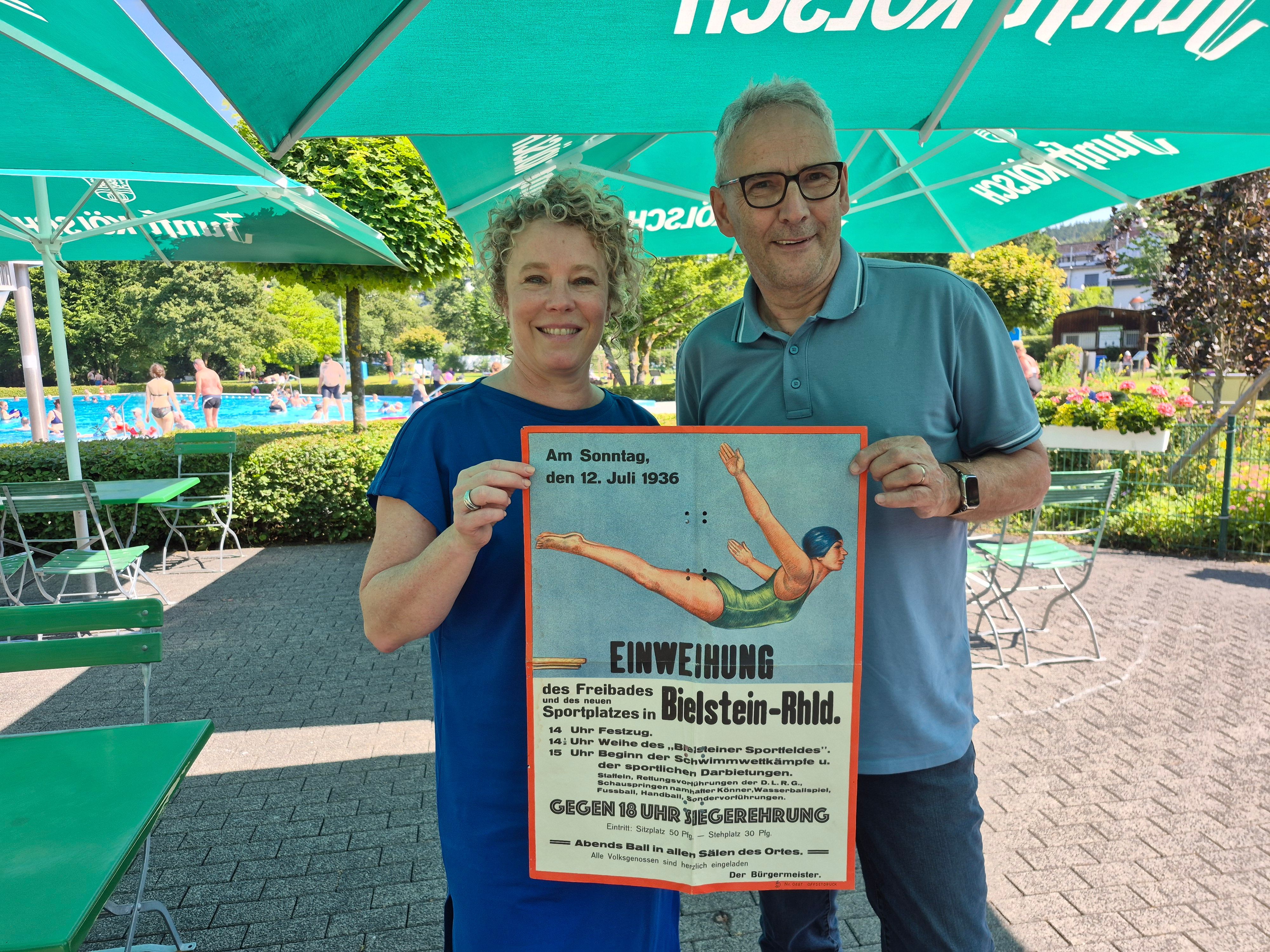 Das Foto zeigt links Nicole Klein und rechts Andreas Zurek mit einem alten Plakat vom Einweihungsfest vor 90 Jahren.