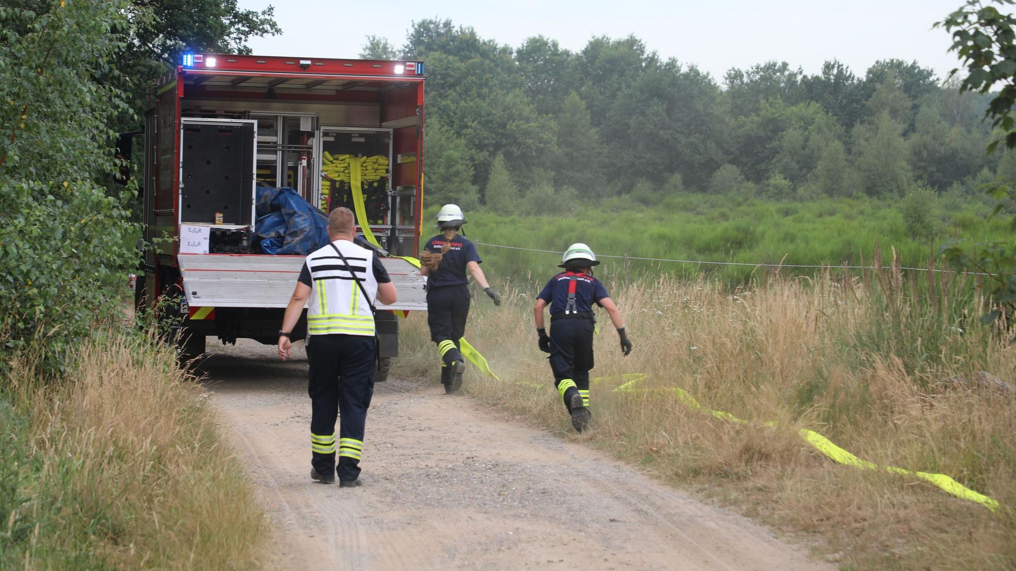 Feuerwehrleute verlegen von einem Schlauchwagen einen B-Schlauch zur Wasserversorgung der Einsatzstelle an einem Waldbrand in der Wahner Heide.