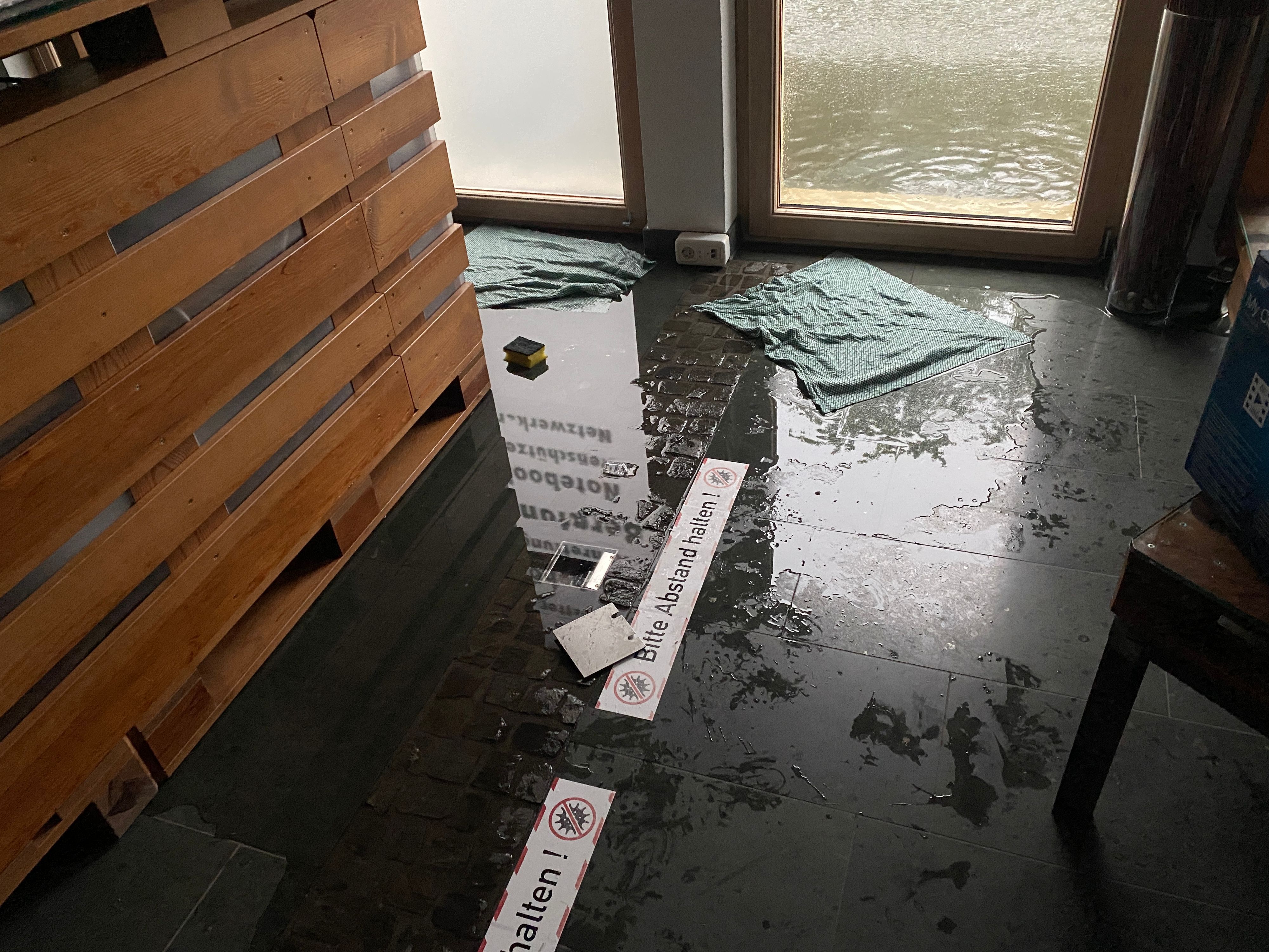 Auf dem Boden vor einer Eingangstür liegen feuchte Aufnehmer, draußen vor der Tür steht das Wassser.