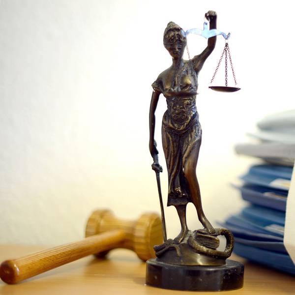 Die modellhafte Nachbildung der Justitia steht in einem Raum eines Richters neben einem Holzhammer und einem Aktenstapel.