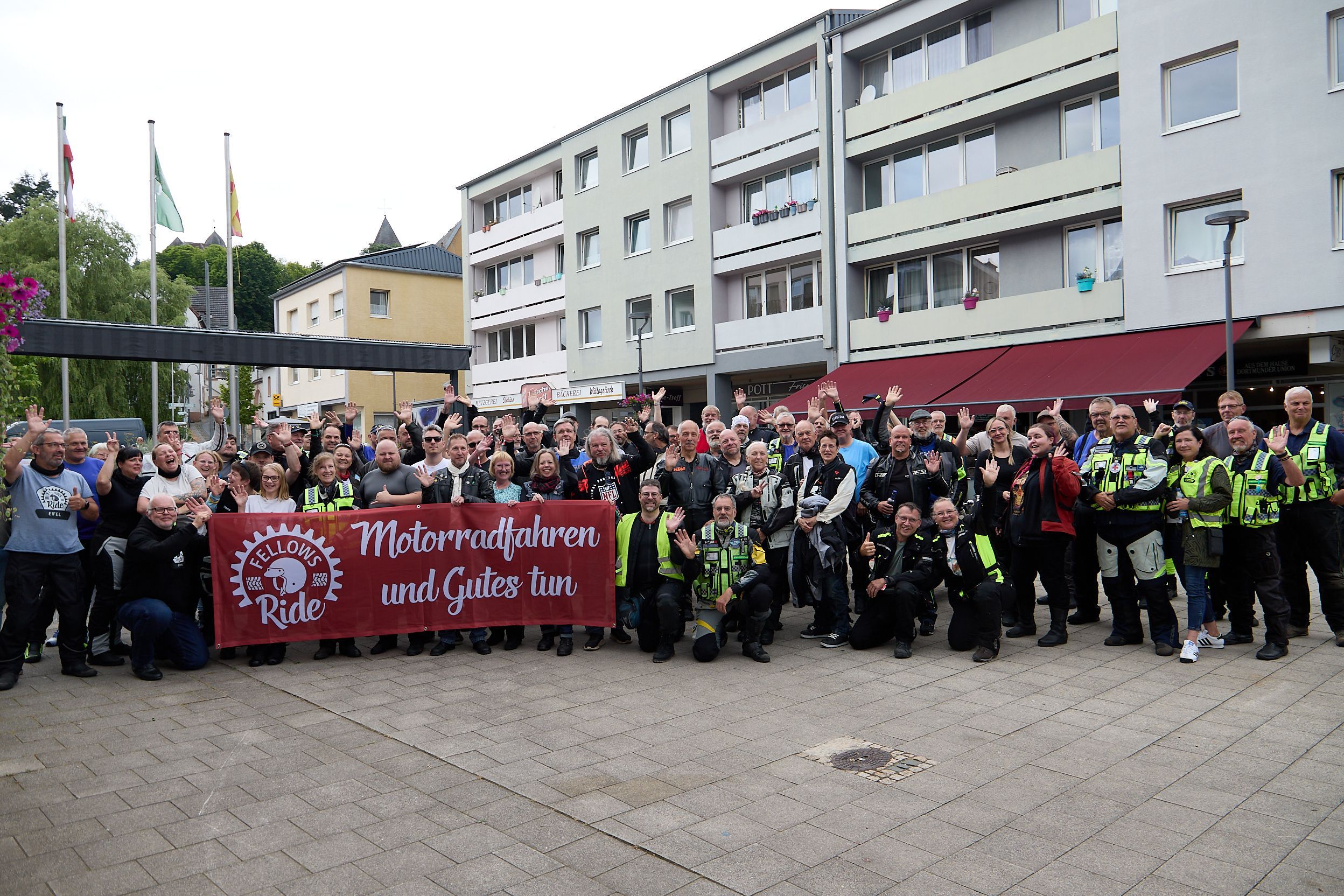 Eine große Gruppe Teilnehmer hat sich mit einem Transparent „Motorradfahren und Gutes tun“ in der Schleidener Innenstadt zum Gruppenbild aufgestellt.