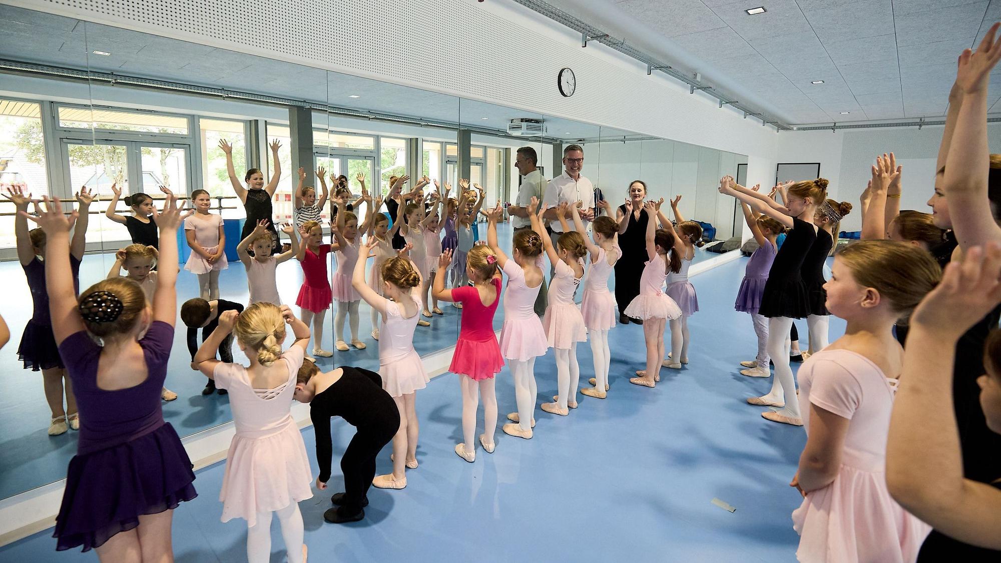 Die jungen Akteure proben vor einem wandfüllenden Spiegel. Der Bürgermeister und die Trainerin schauen zu.