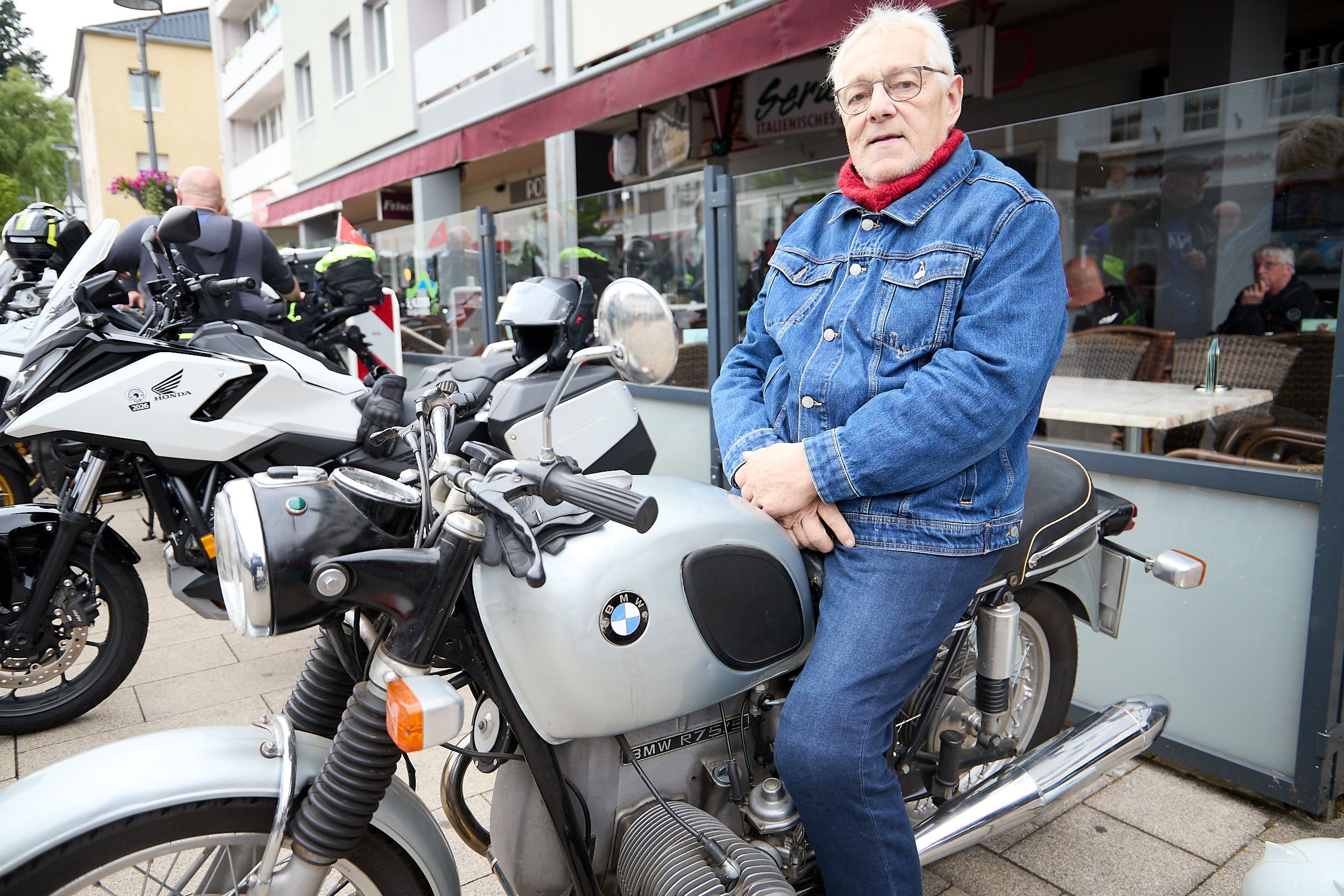 Der grauhaarige Mann sitzt in Jeans-Kluft auf einem BMW-Motorrad.