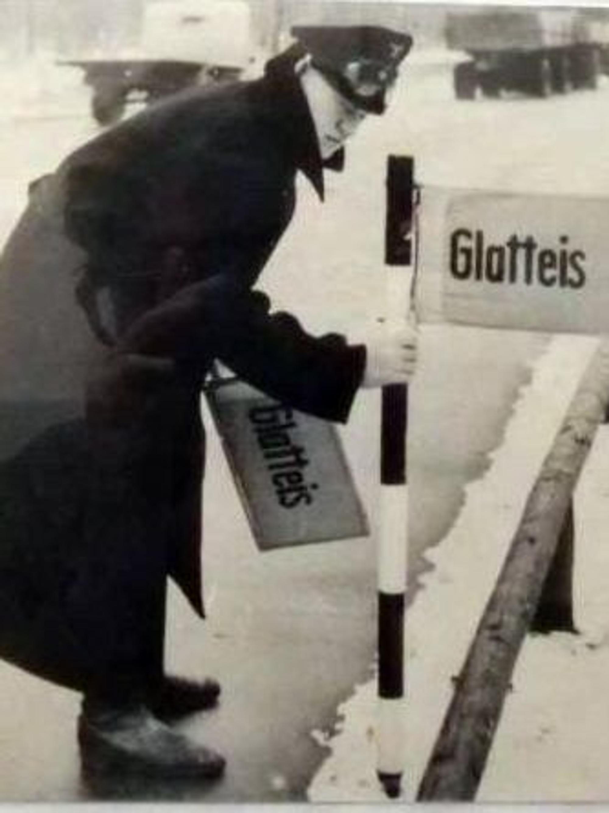 Ein Straßenwärter steckt ein Schild mit der Aufschrift „Glatteis“ in den Schnee am Fahrbahnrand der A4.