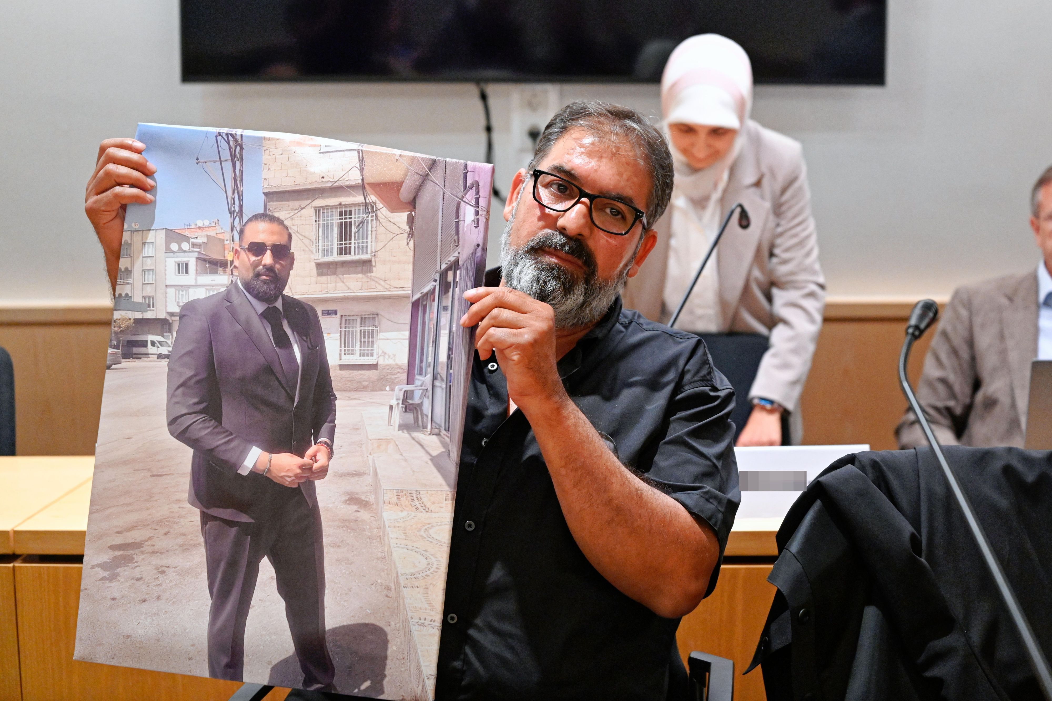 Erdal Calar (vorn), Vater des getöteten Zugbegleiters Serkan Calar, hält im Verhandlungssaal des Landgerichts ein Bild des Opfers in den Händen.