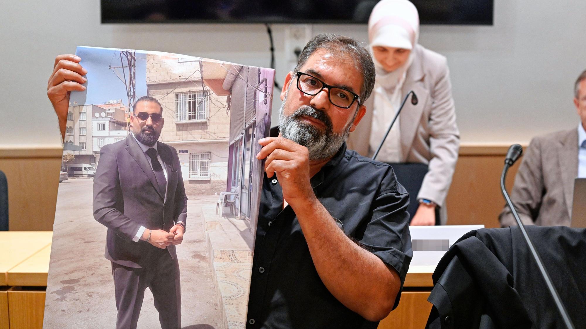 Erdal Calar (vorn), Vater des getöteten Zugbegleiters Serkan Calar, hält im Verhandlungssaal des Landgerichts ein Bild des Opfers in den Händen.