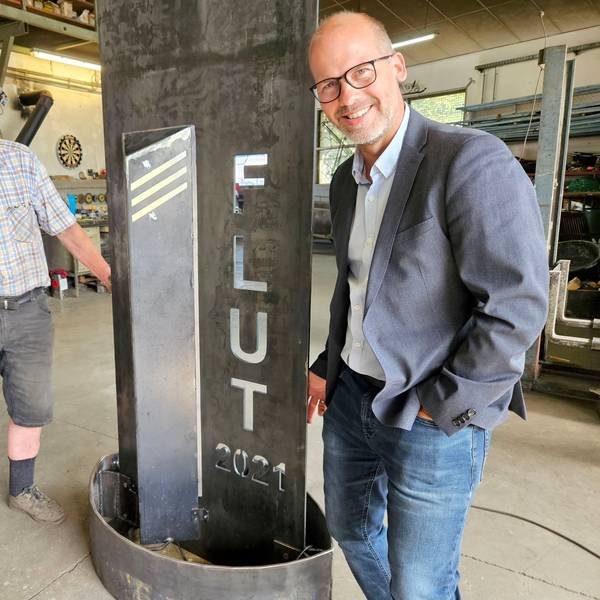 Zwei Männer stehen neben einer Metallstele, in die „Flut 2021“ eingraviert ist.