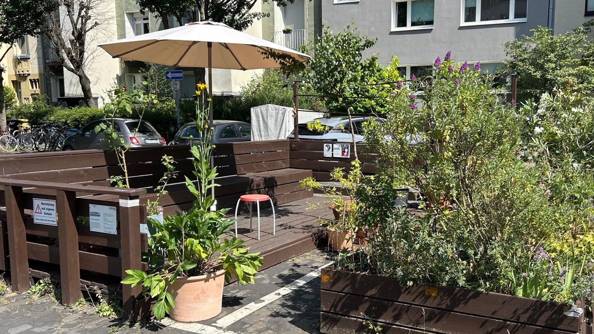 Ein Sonnenschirm und Pflanzen umrahmen Sitzplätze auf einer Straße.