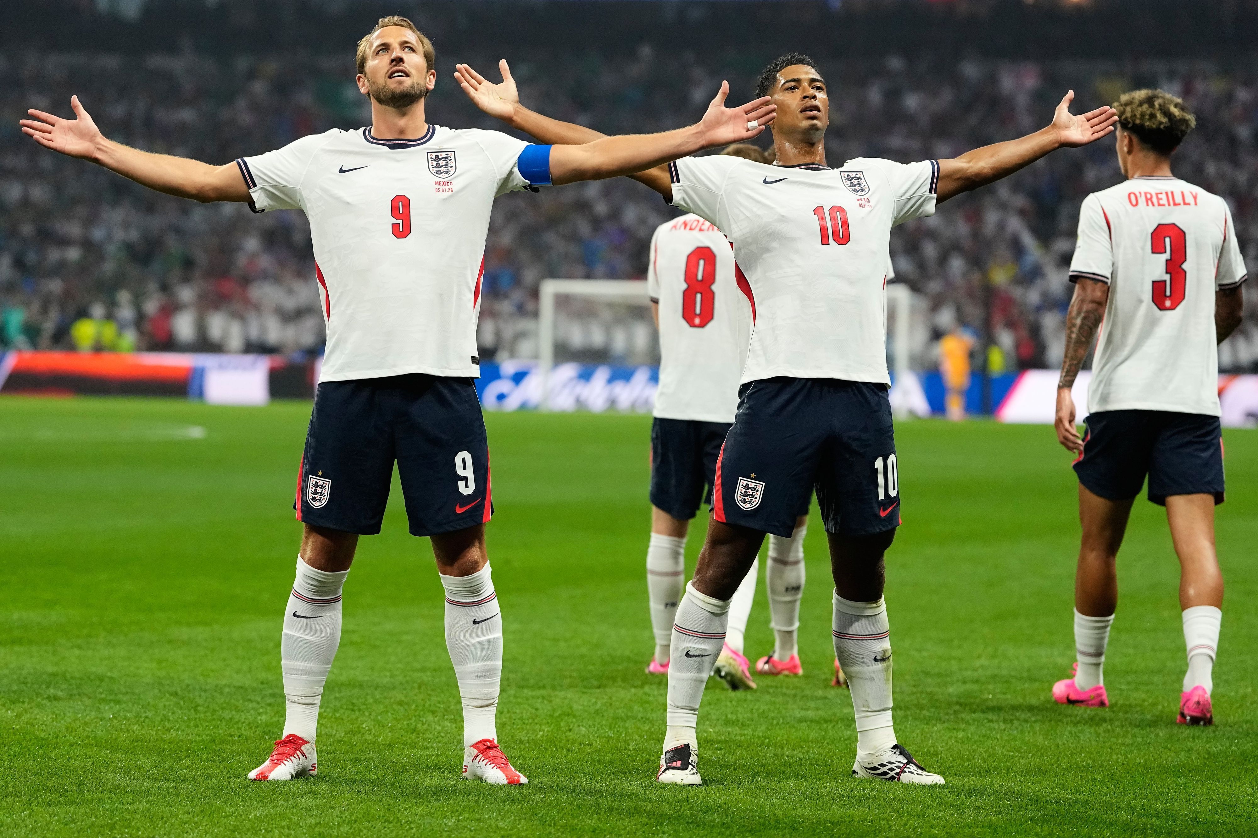 Kane und Bellingham stehen im England-Dress auf dem Platz und jubeln.