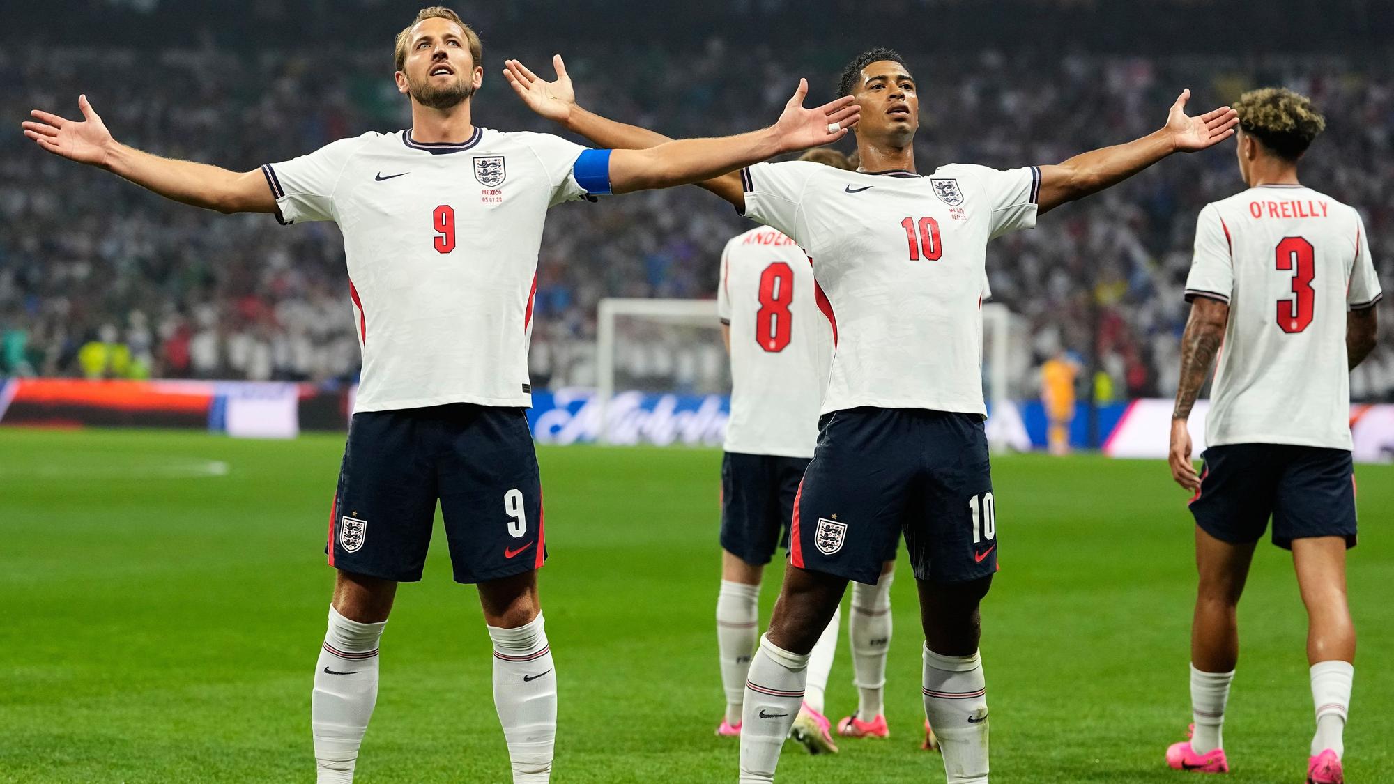 Kane und Bellingham stehen im England-Dress auf dem Platz und jubeln.