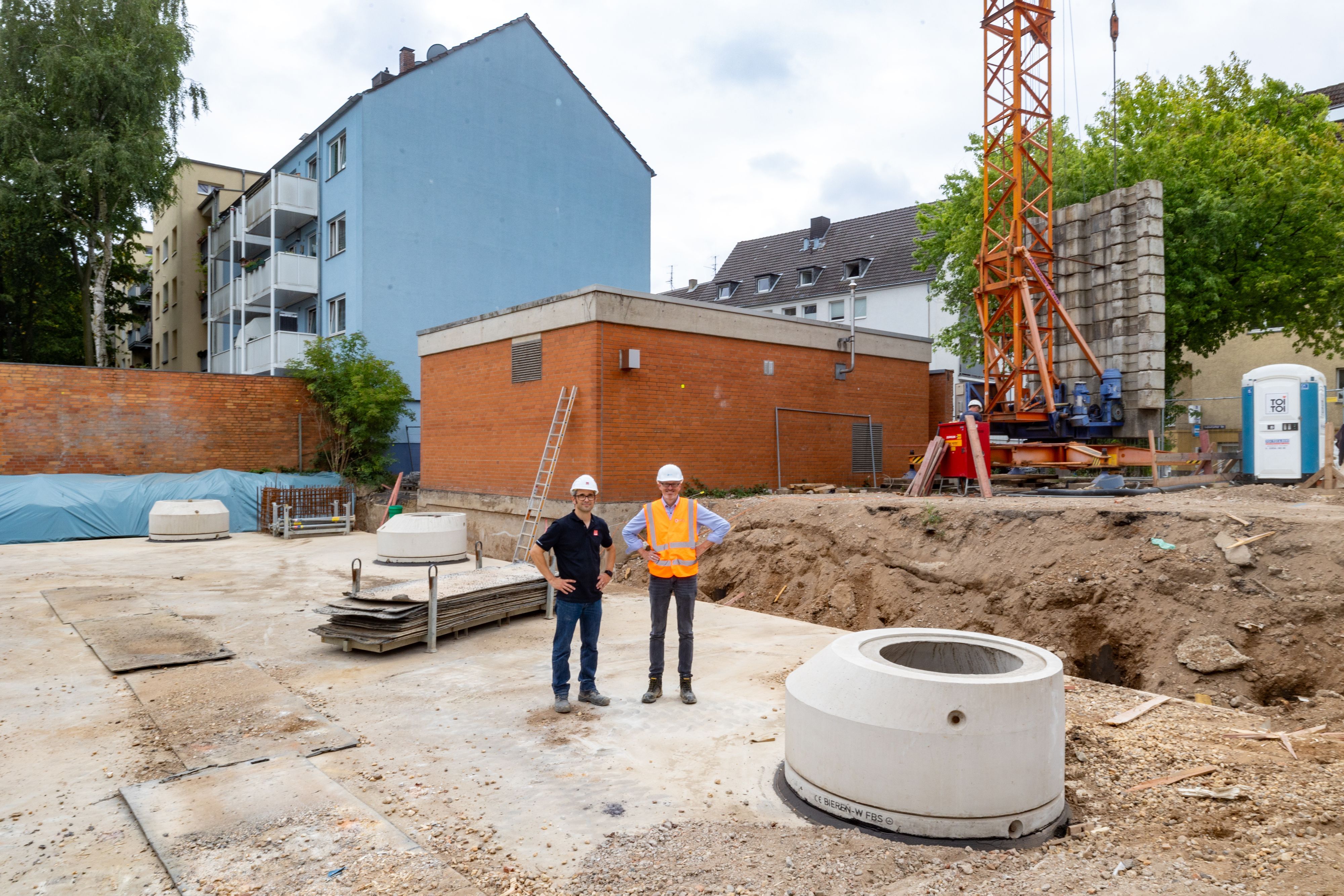 Zwei Männer mit Bauhelmen stehen auf einem großen Betondeckel, es ist das neue Regenrückhaltebecken.