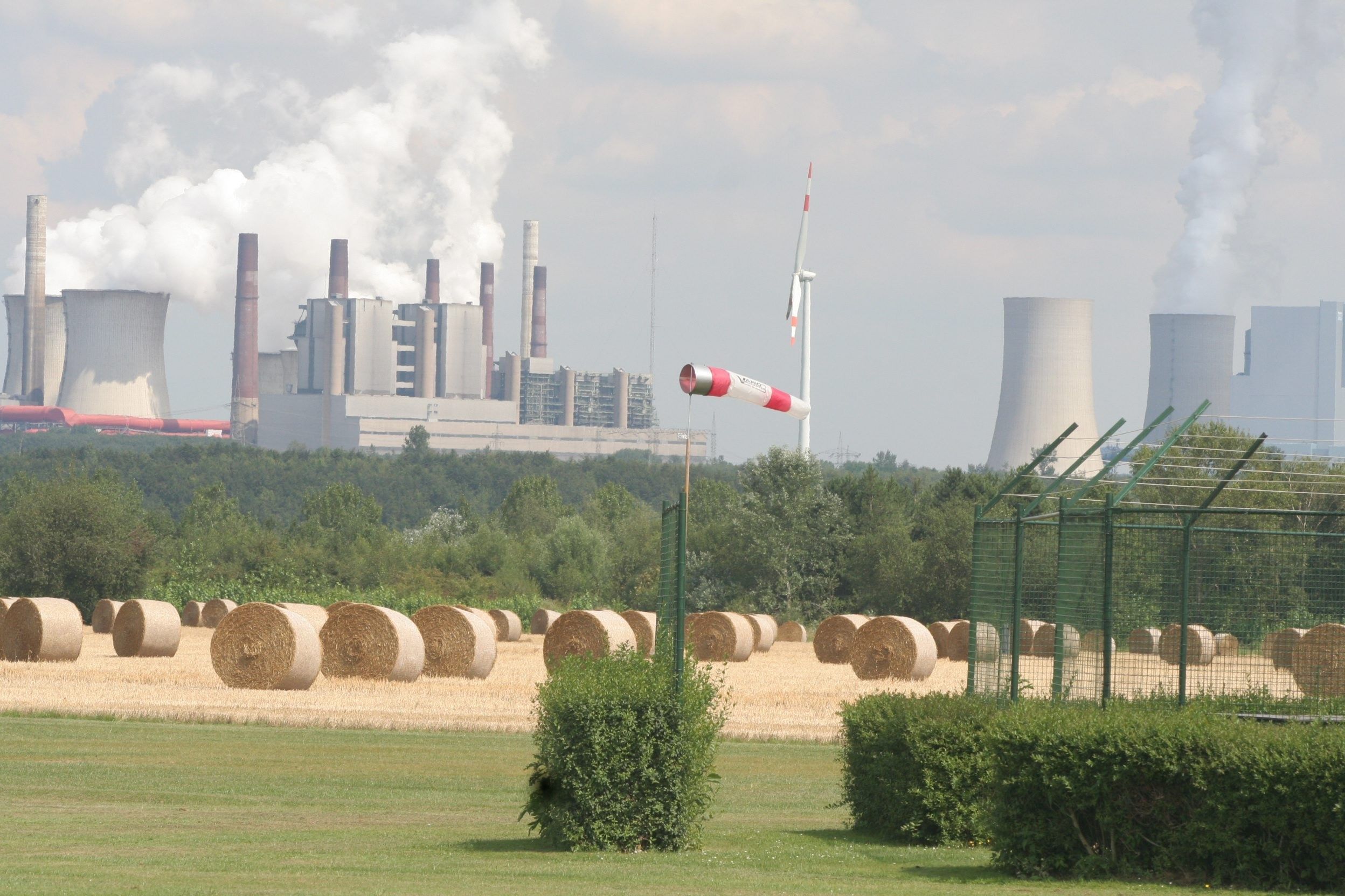 Das Bild zeigt ein Feld mit Strohballen vor der Kraftwerkskulisse.